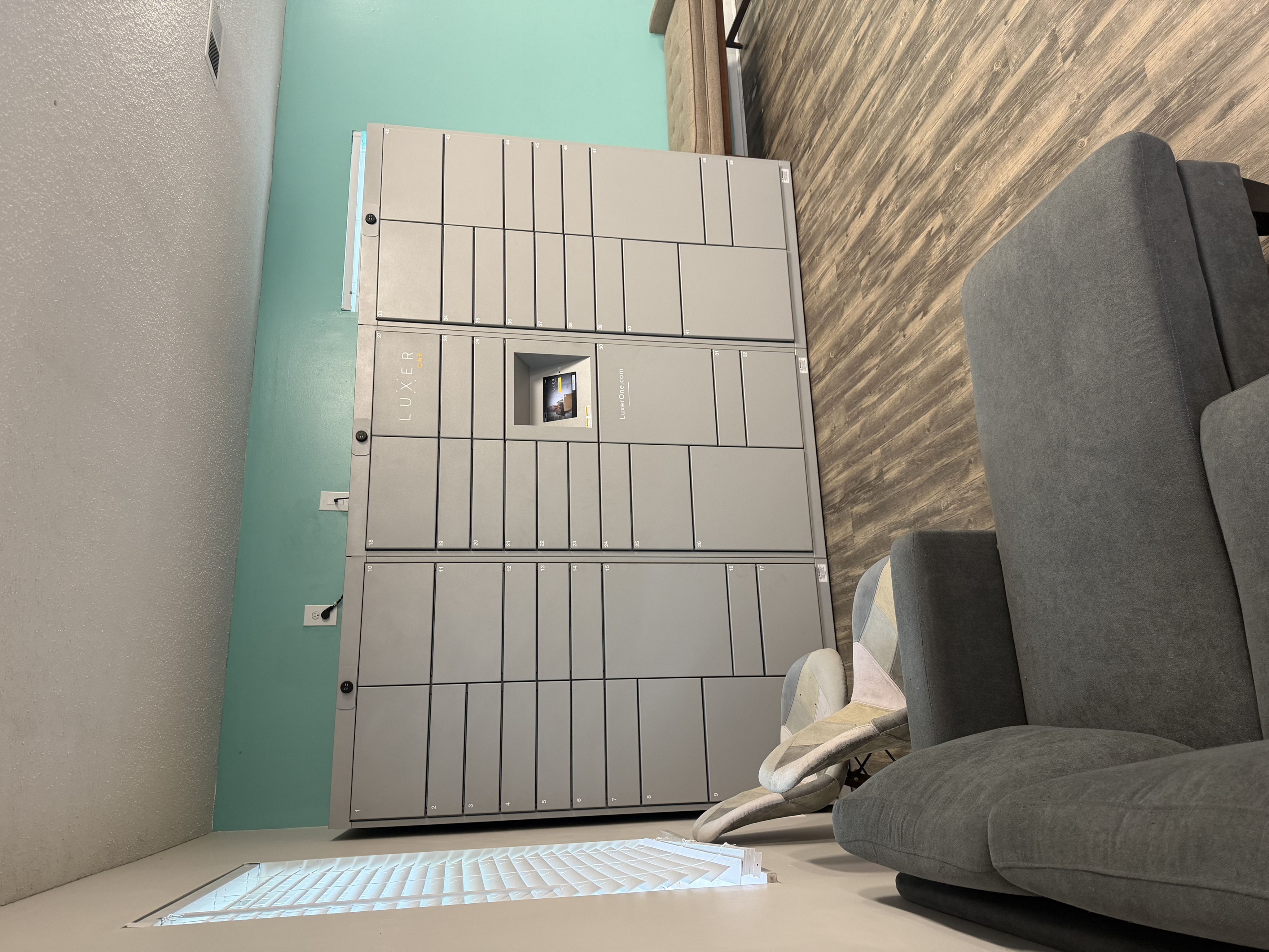 Contemporary apartment lobby with sleek gray package lockers, cozy seating area, and warm wood flooring.