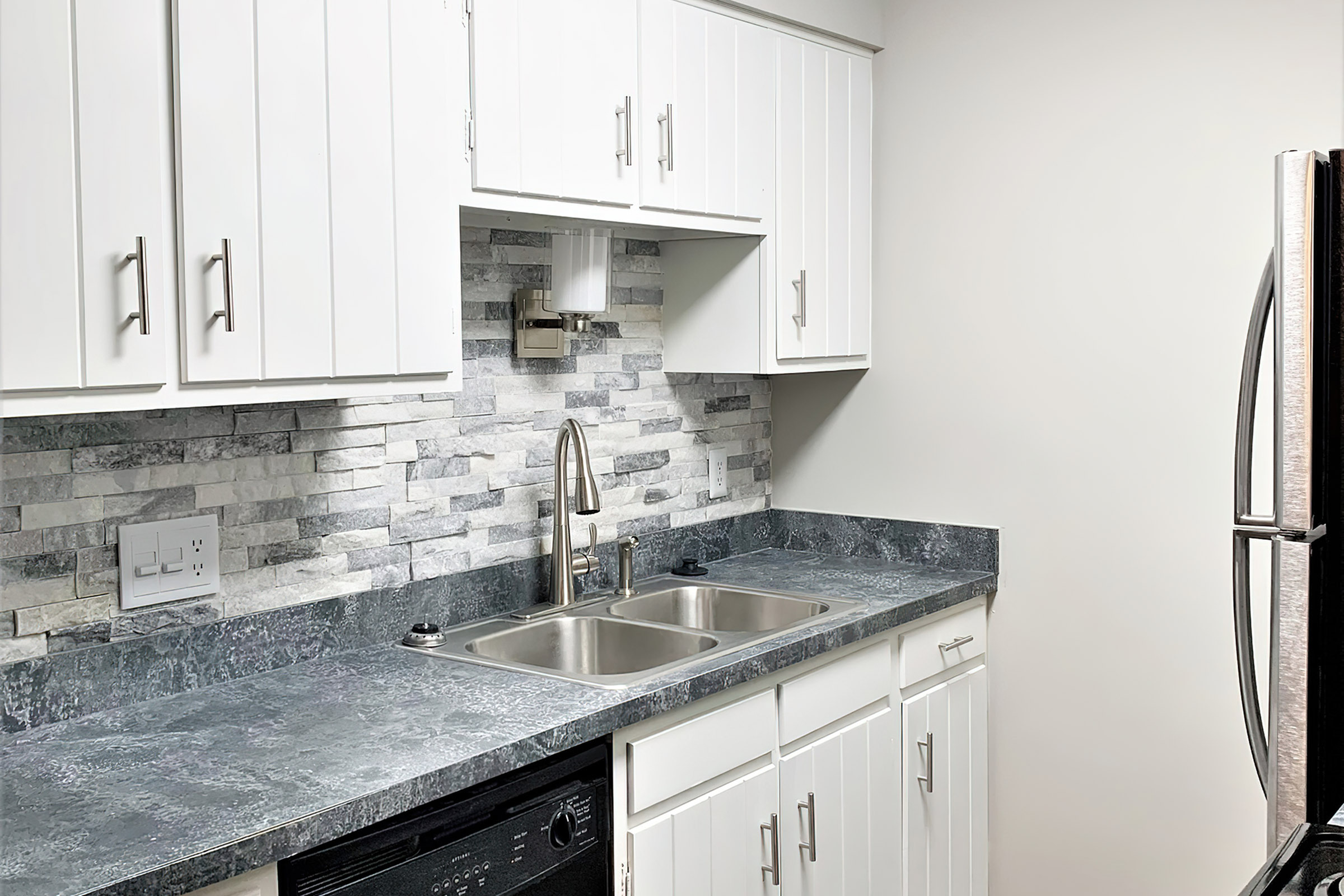 Modern kitchen featuring sleek white cabinets, elegant stone backsplash, and spacious dual sink.