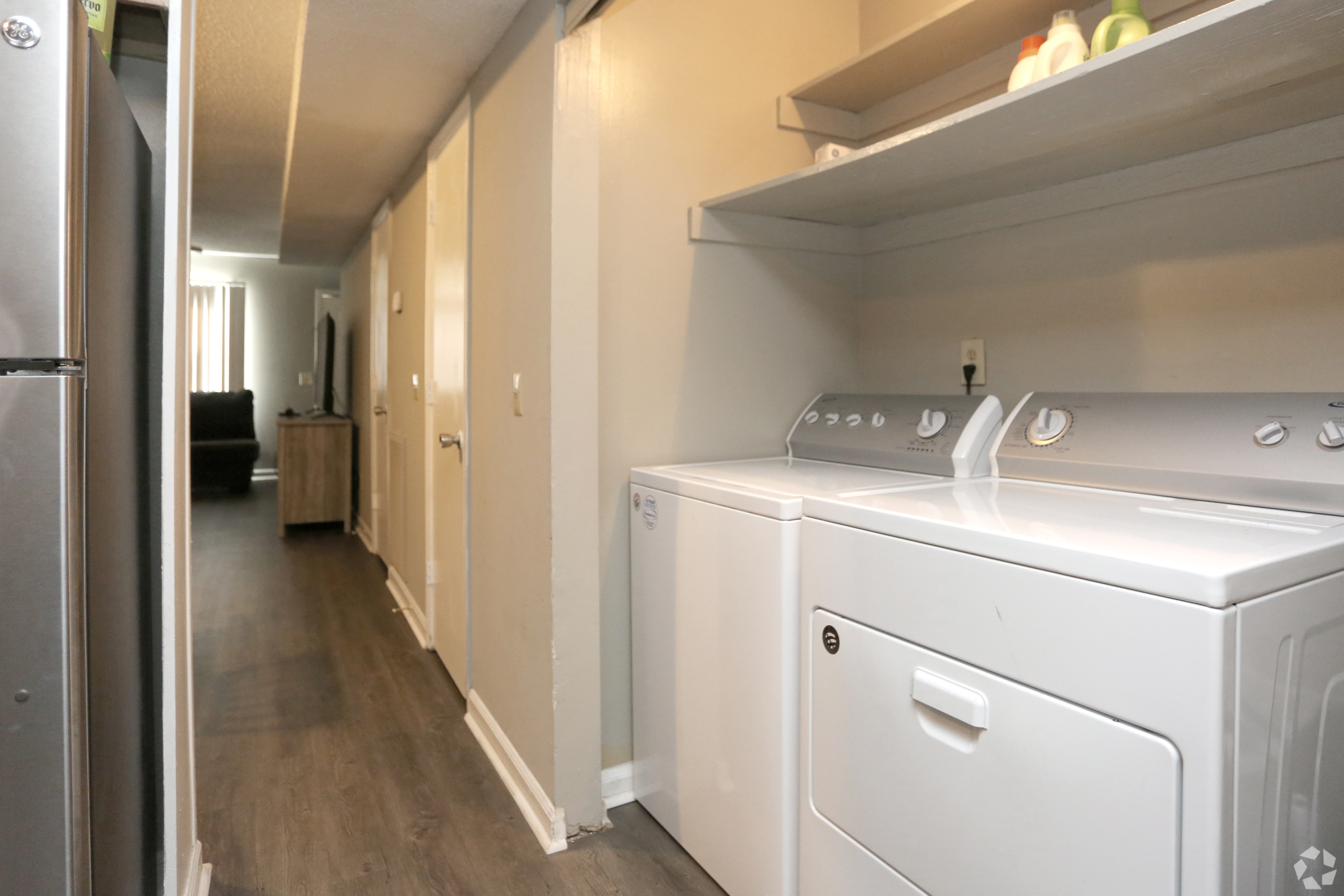 Modern apartment hallway with sleek hardwood floors, featuring an in-unit washer and dryer set with convenient shelving above.