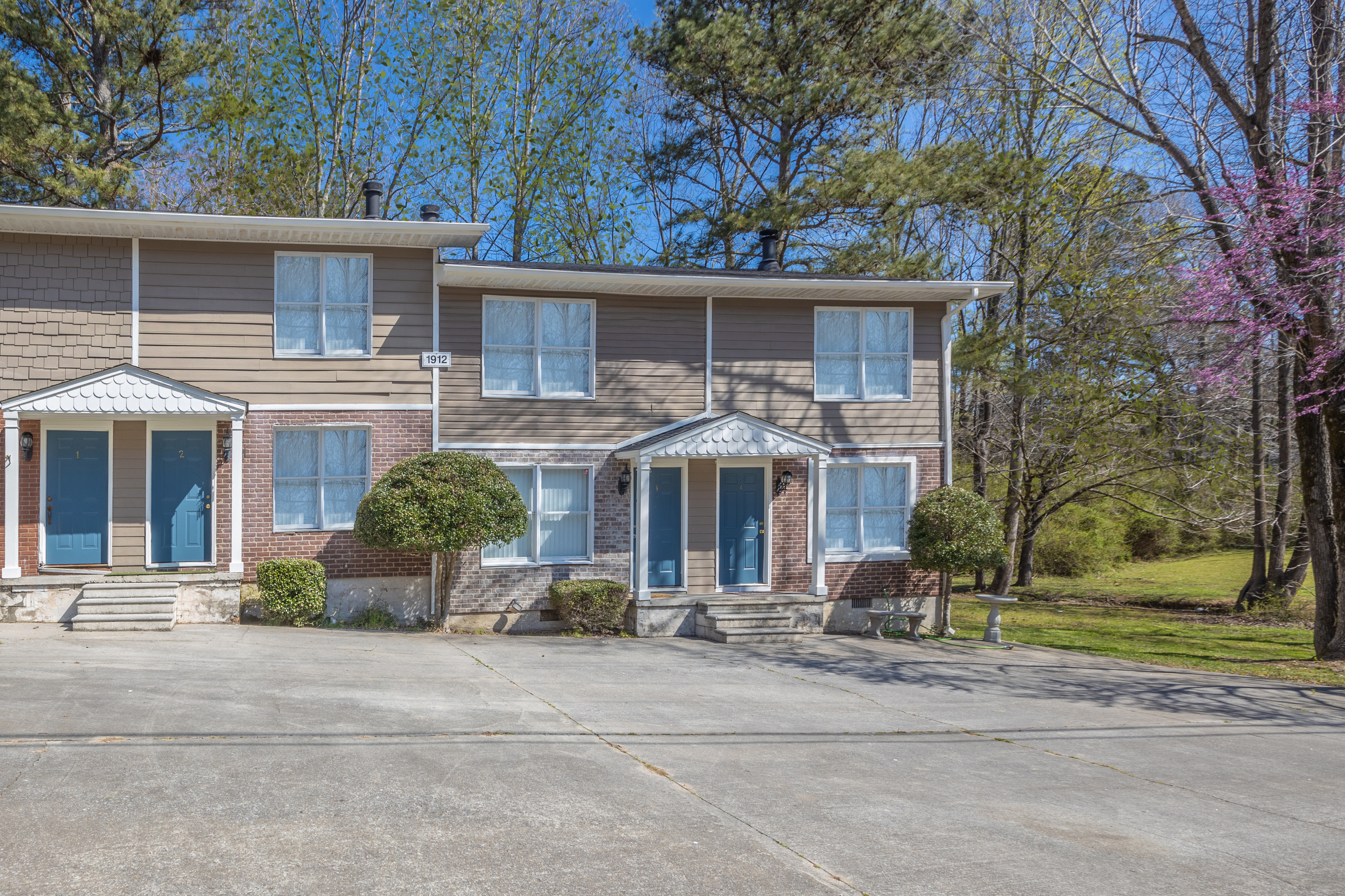Charming townhouse with classic brick facade and blue doors, surrounded by lush greenery and mature trees.