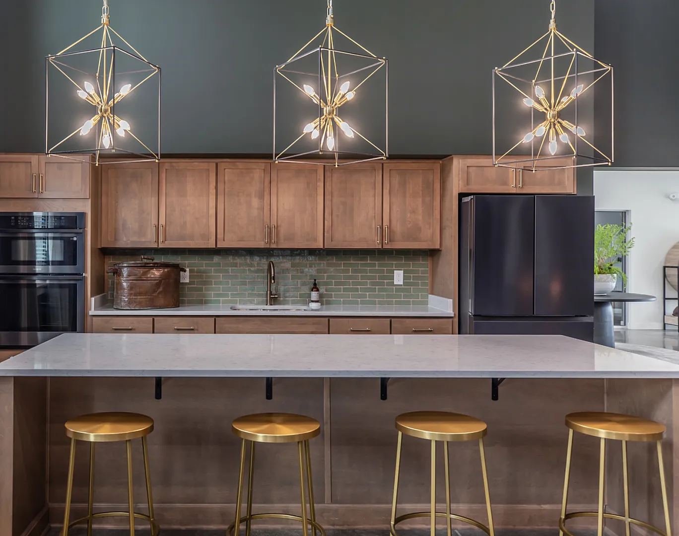 Modern kitchen with elegant pendant lighting, chic wooden cabinets, and sleek black appliances, featuring a stylish island with gold stools.