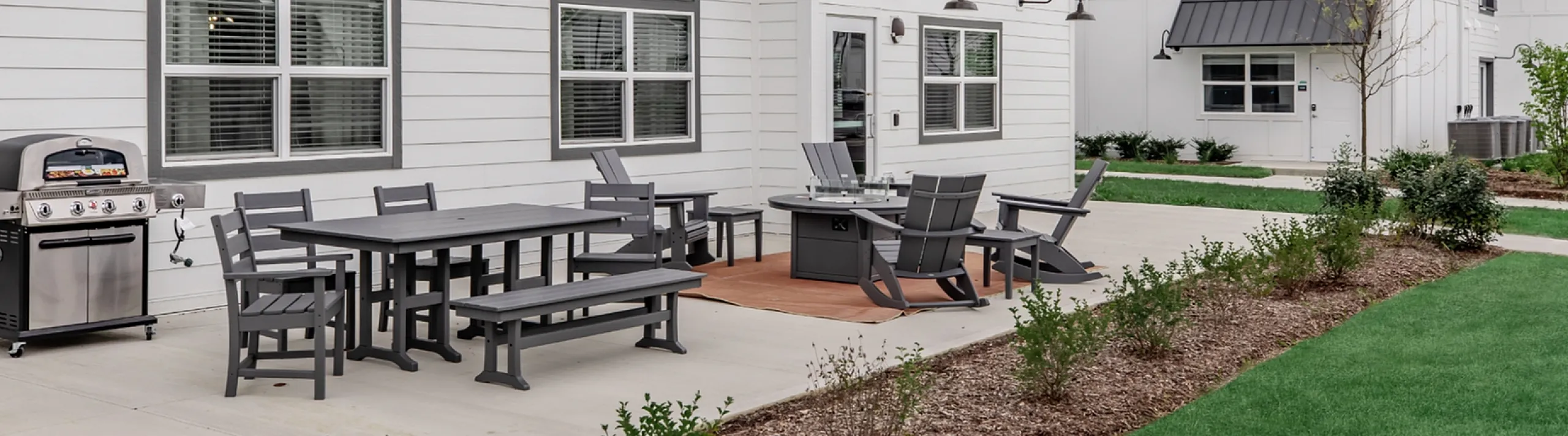 Charming outdoor patio area with stylish seating and modern grill, perfect for entertaining in a contemporary white-clad apartment building.