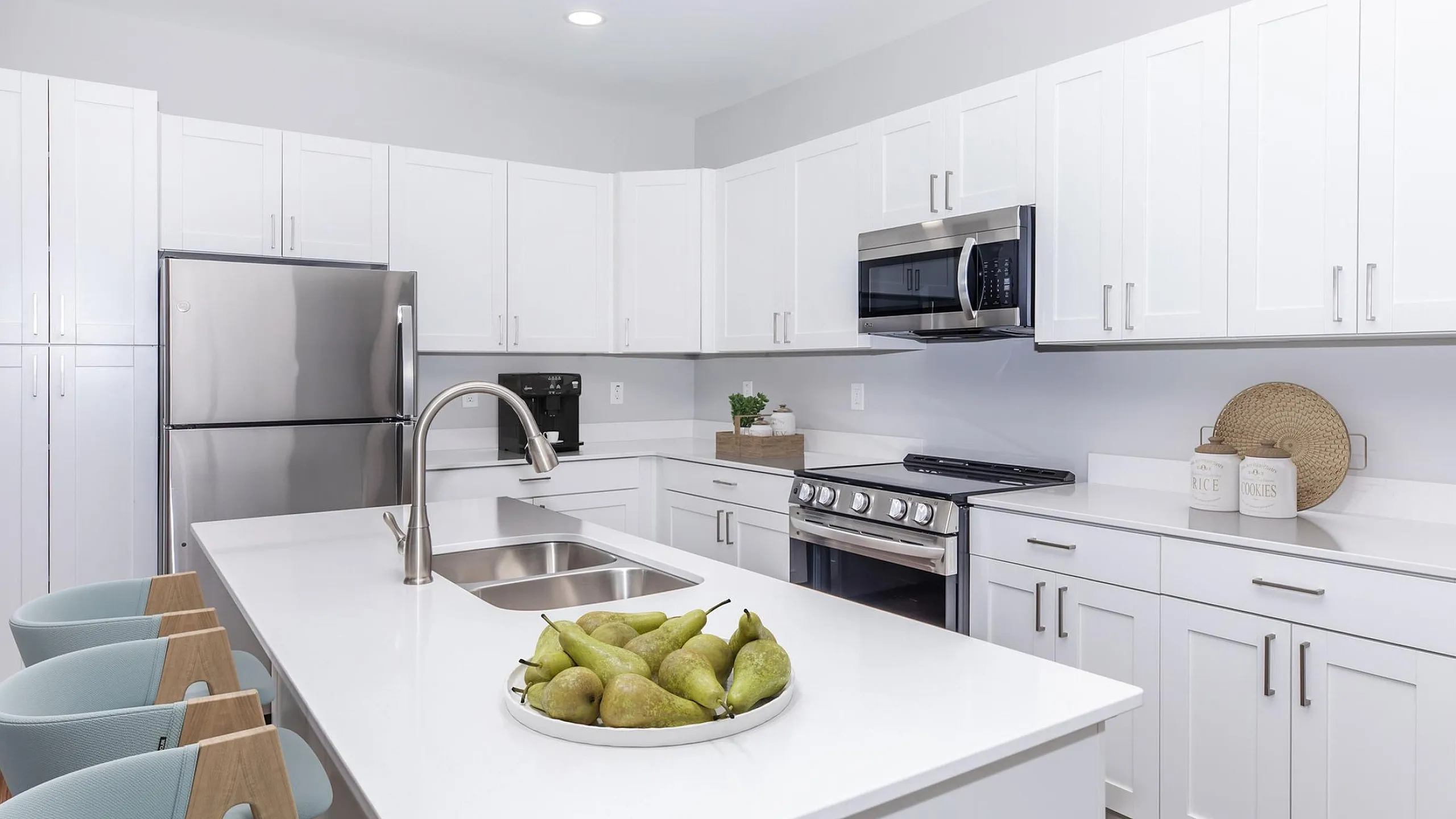 Modern kitchen with sleek white cabinetry, stainless steel appliances, and an inviting island with elegant bar stools and decorative fruit bowl.
