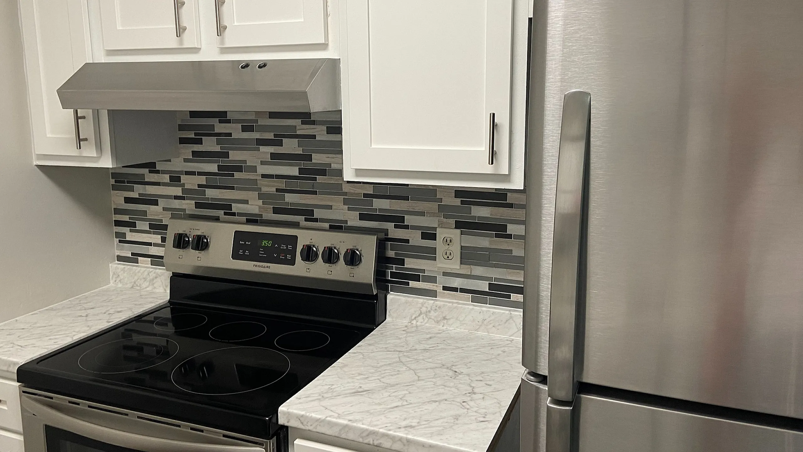 Modern kitchen with stainless steel appliances, sleek white cabinetry, and a stylish mosaic backsplash.