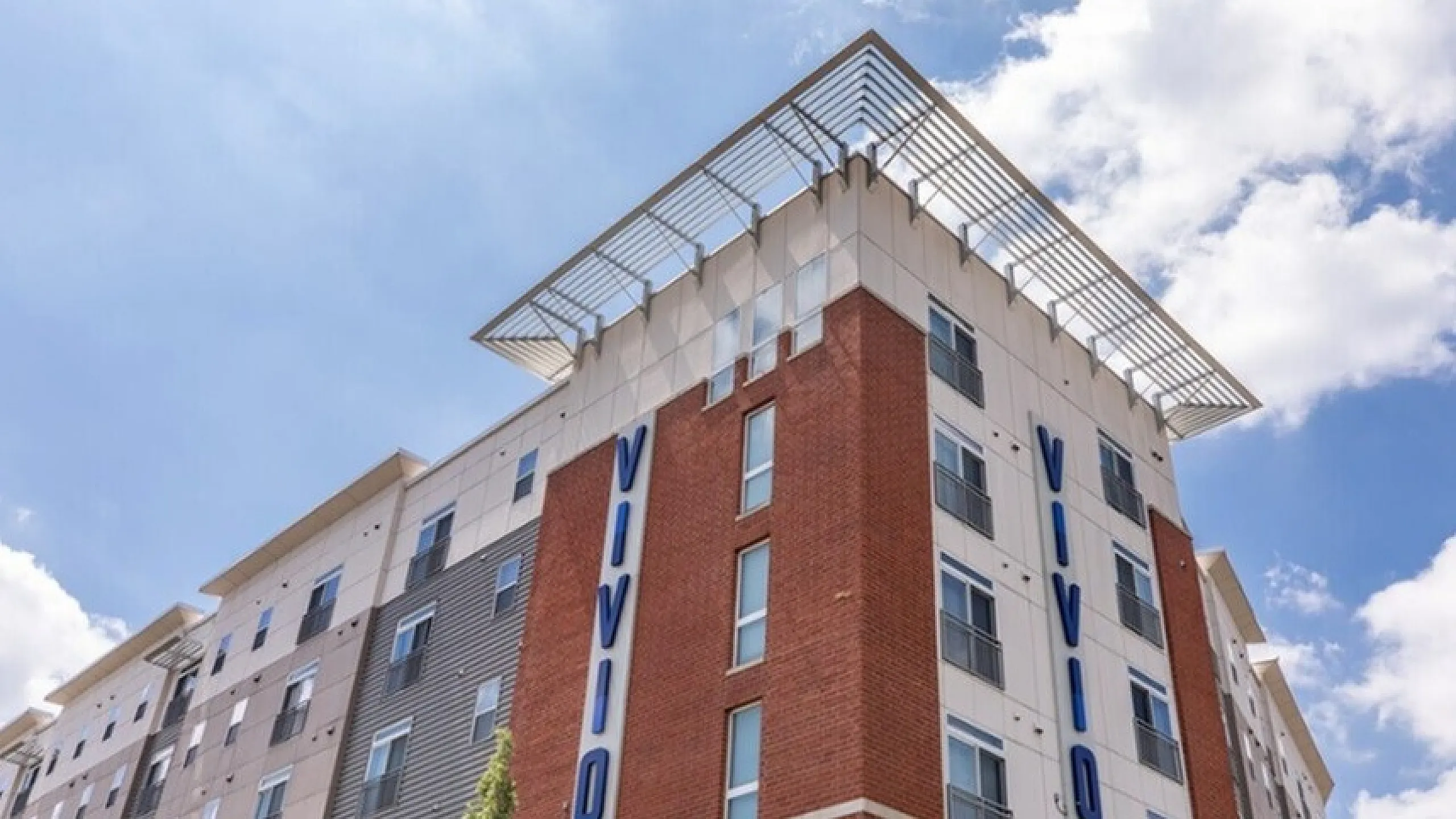 Modern urban apartment building with striking architecture under a vibrant blue sky, featuring brick and paneled exterior with bold signage.