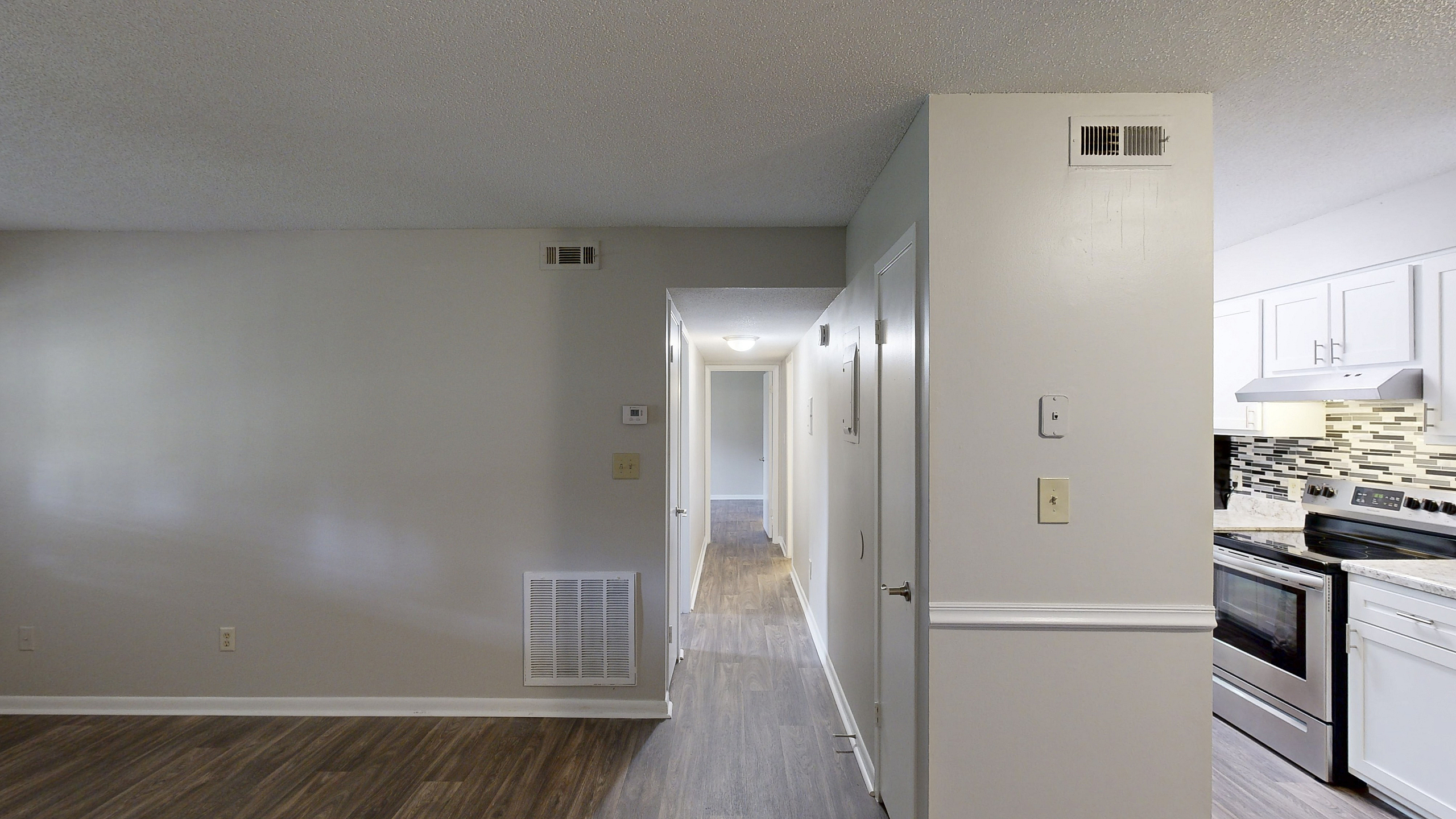 Modern apartment interior featuring sleek laminate flooring, a bright hallway leading to spacious rooms, and a stylish kitchen with contemporary backsplash and stainless steel appliances.