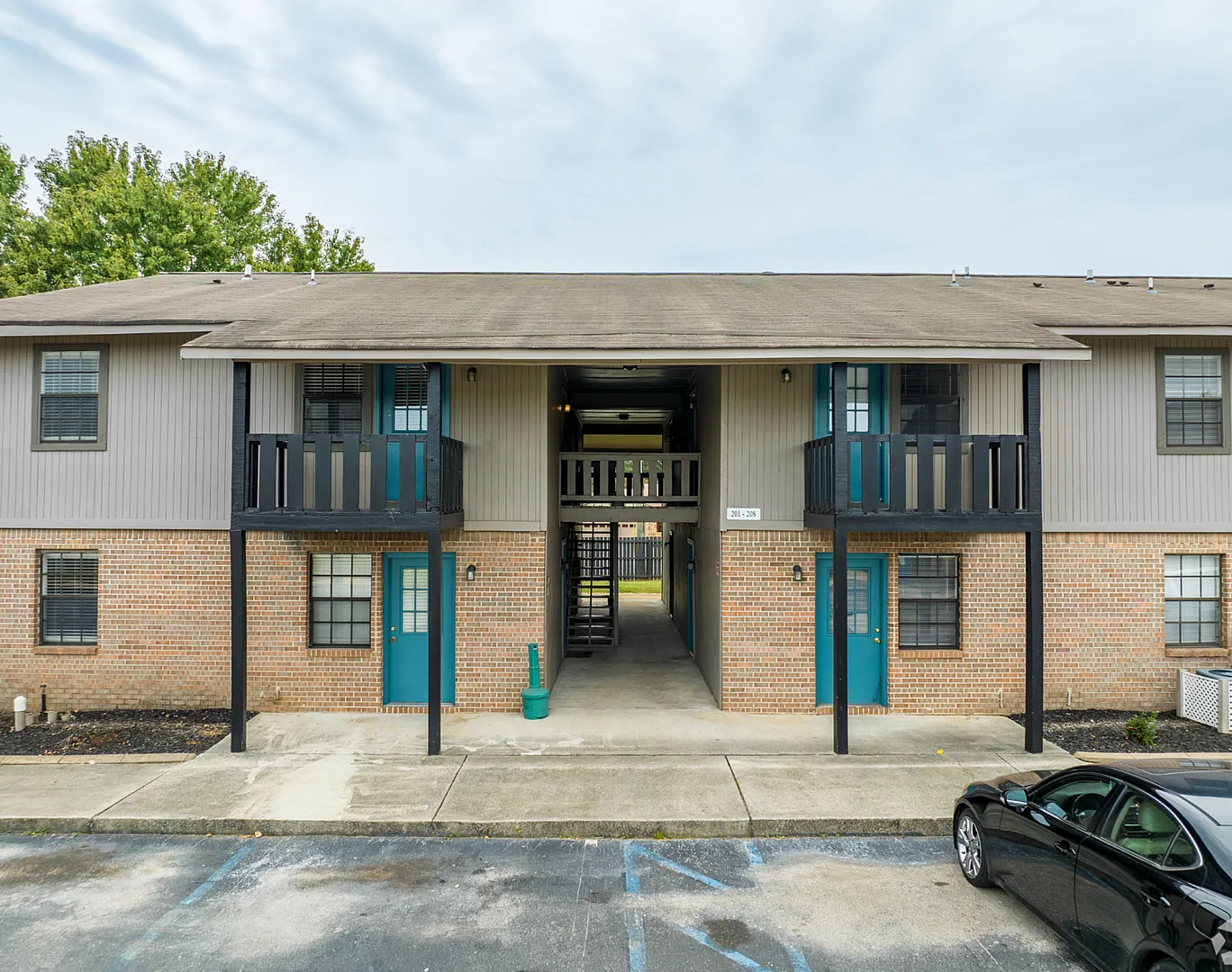 Charming two-story apartment building with private balconies and vibrant teal doors, surrounded by lush greenery.
