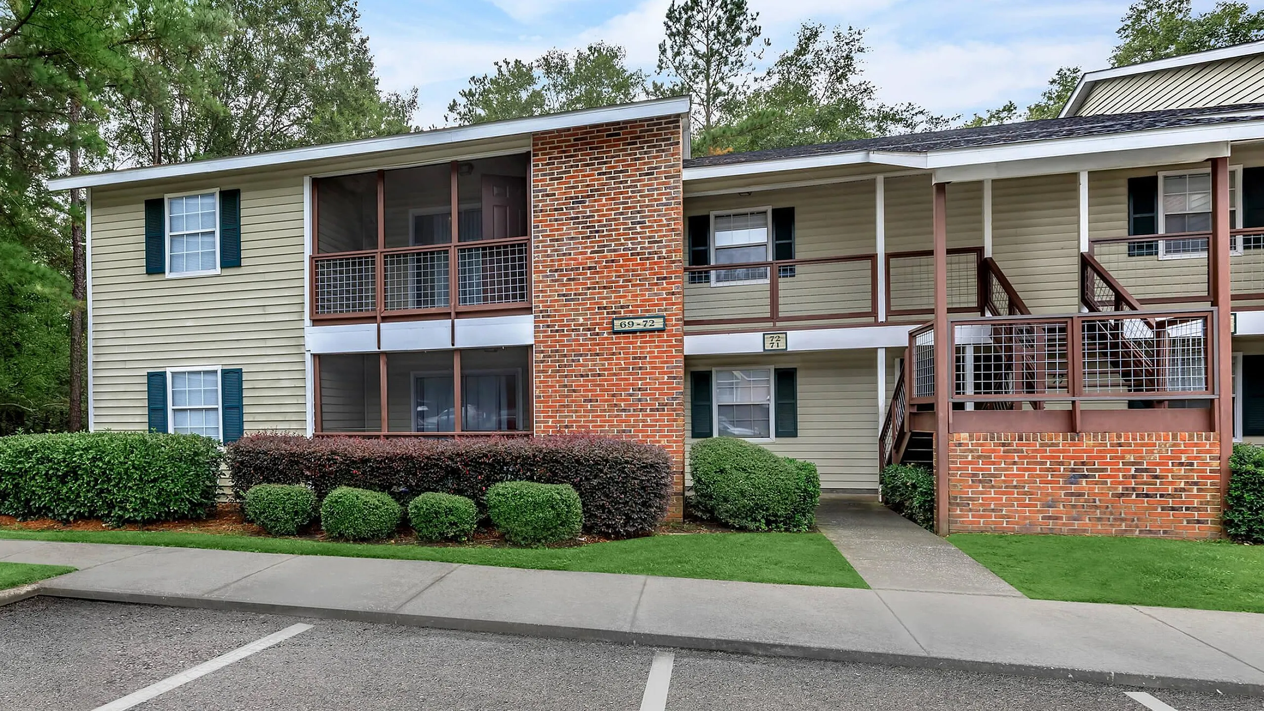Charming apartment building featuring two levels with private balconies, surrounded by lush greenery and ample parking space.
