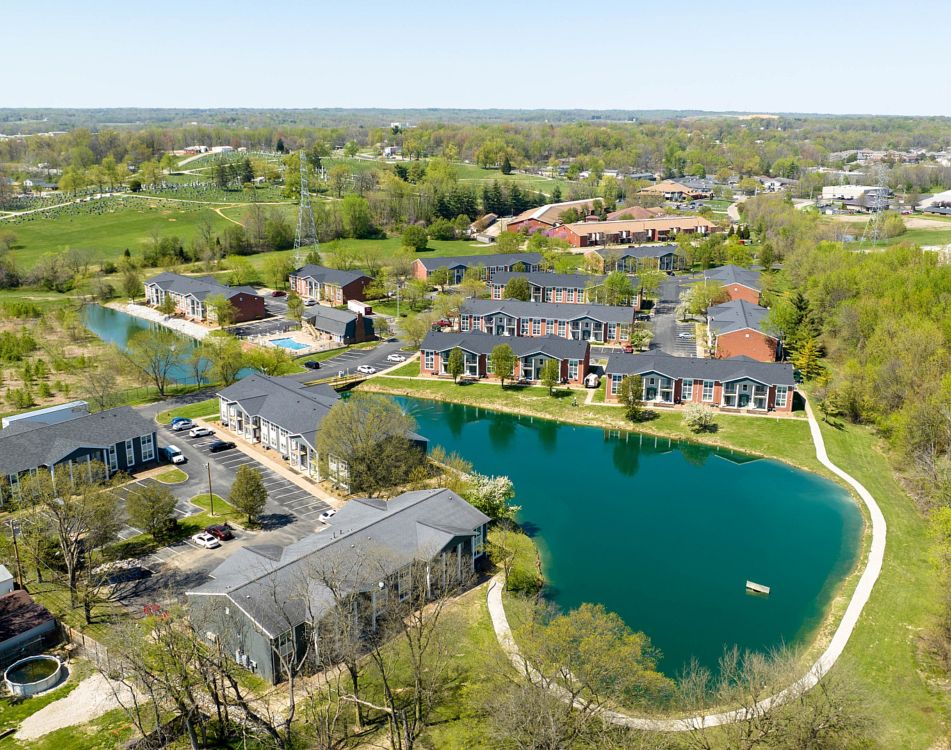Scenic aerial view of a picturesque apartment complex nestled among lush greenery and a serene lake, offering a tranquil living environment.