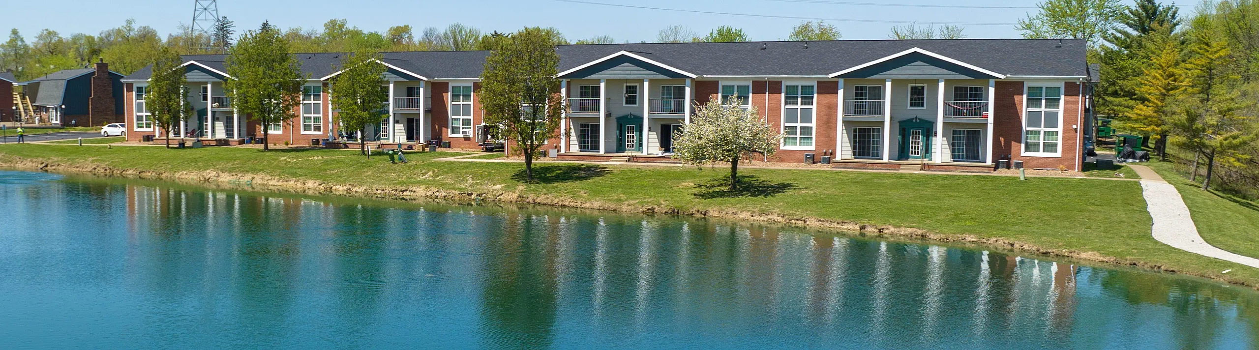 Charming lakeside apartment building with brick facade and scenic landscape, offering serene water views and lush greenery.