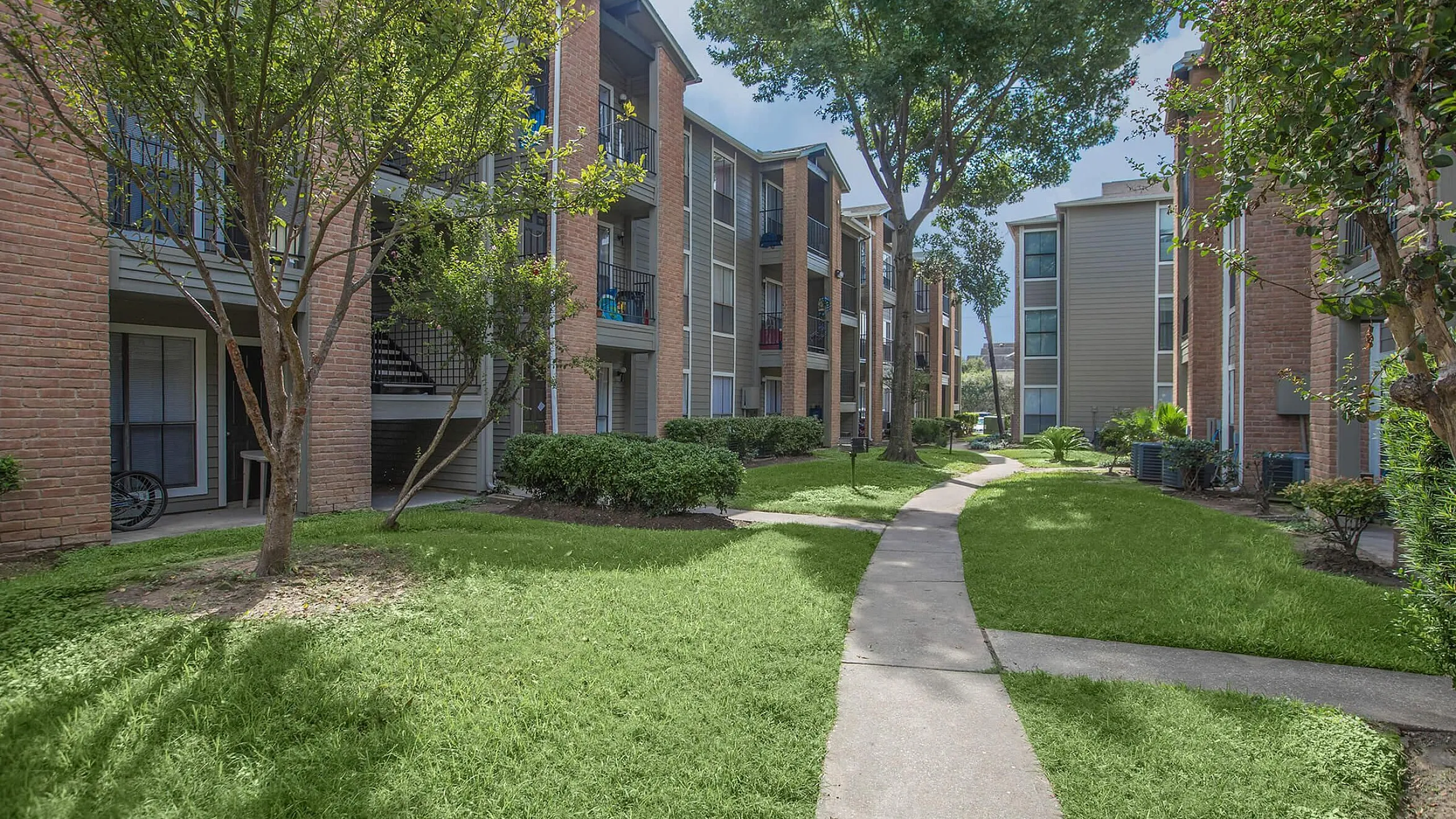 Charming apartment complex with lush landscaping, brick facades, and inviting outdoor pathways.