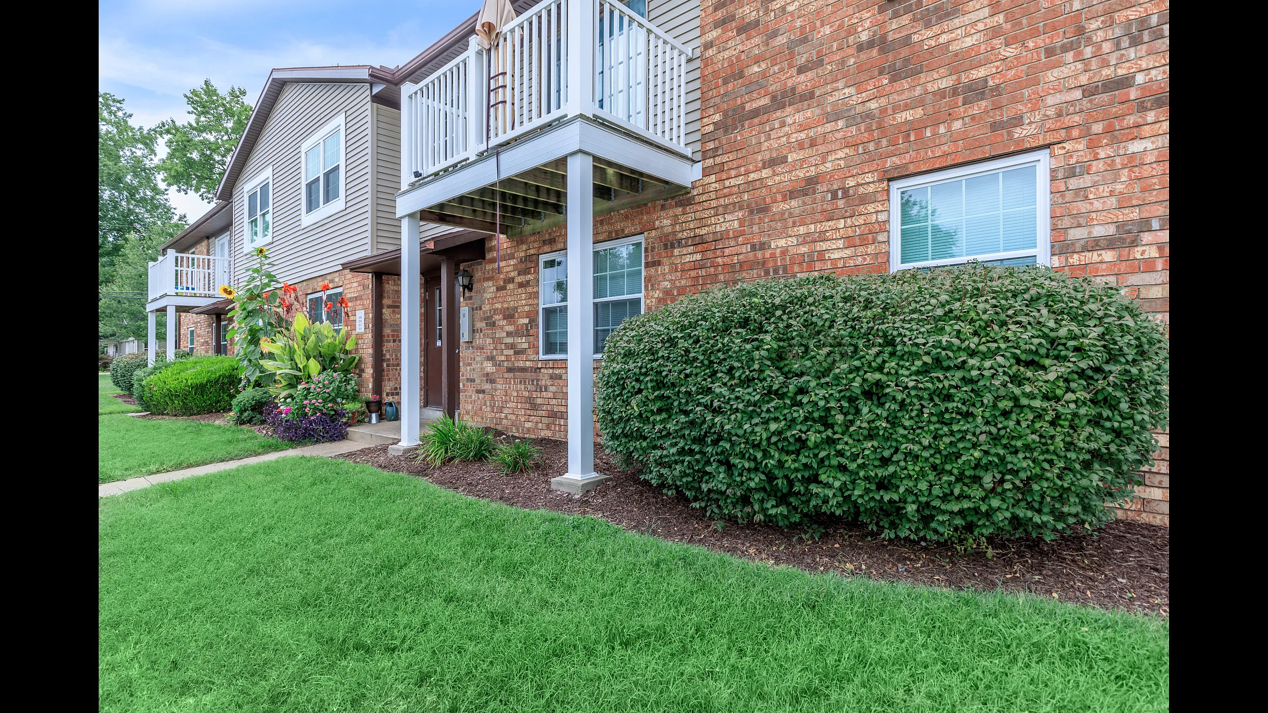 Charming brick apartment building with lush landscaping and inviting front porches.