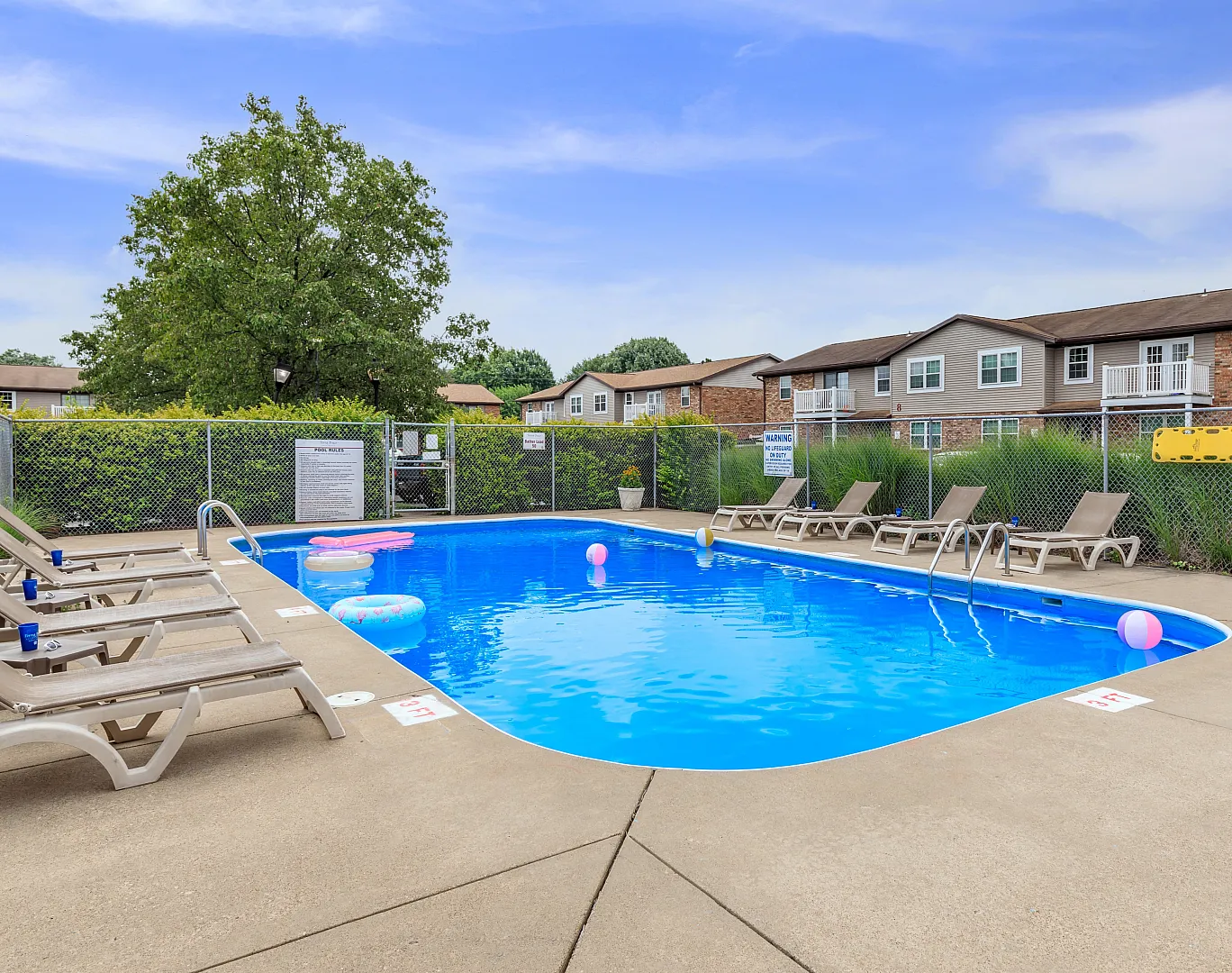 Inviting outdoor pool area with lounge chairs and inflatables, surrounded by greenery and charming residential buildings.