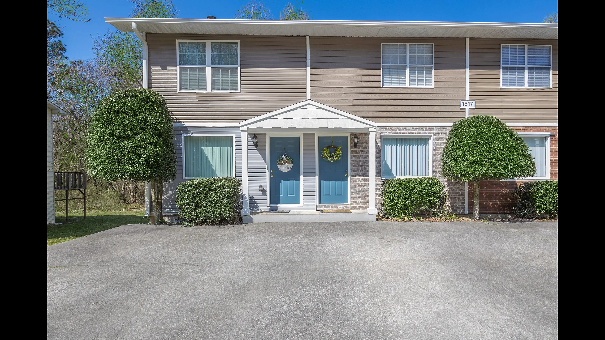 Charming townhouse with dual blue doors, manicured shrubs, and a bright exterior, offering a welcoming and stylish curb appeal.