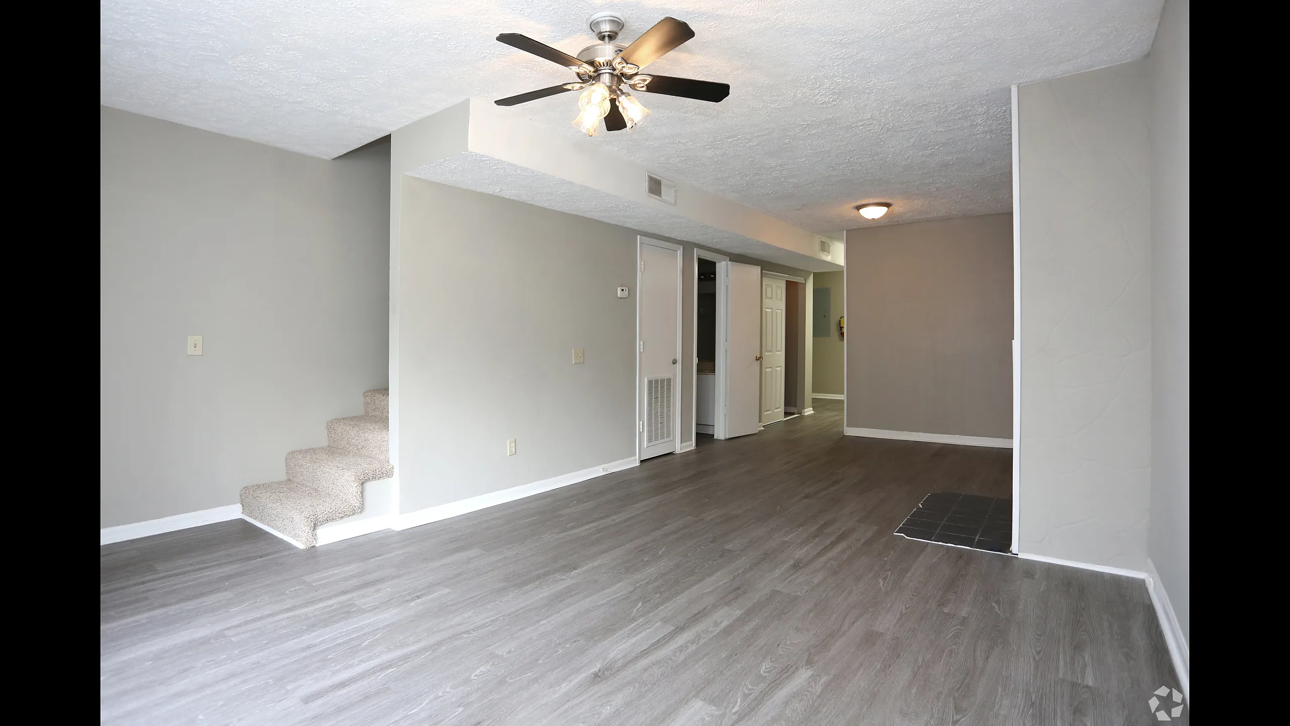 Bright and spacious living room featuring elegant laminate flooring, neutral tones, and modern ceiling fan, with a charming staircase leading to the upper level.