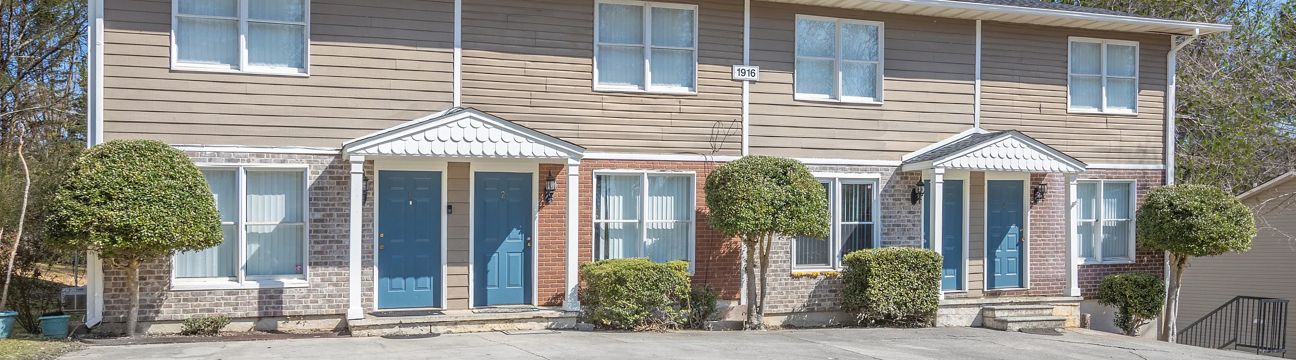 Charming duplex exterior with two blue doors and manicured landscaping under a clear blue sky.