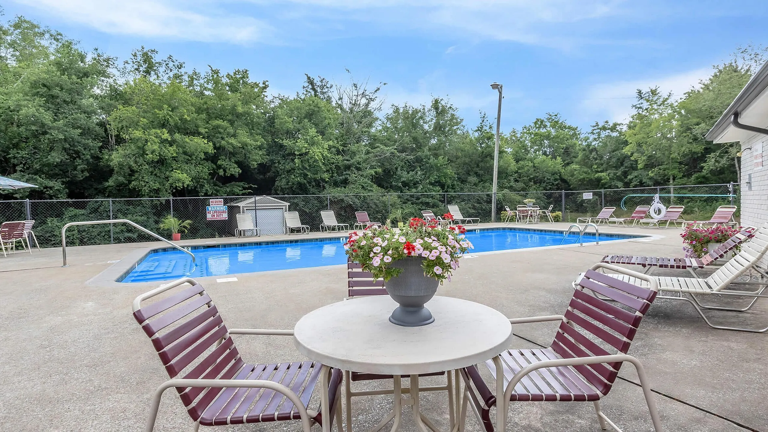 Inviting outdoor pool area with lush greenery, stylish lounge chairs, and a charming table with floral centerpiece, perfect for relaxation.