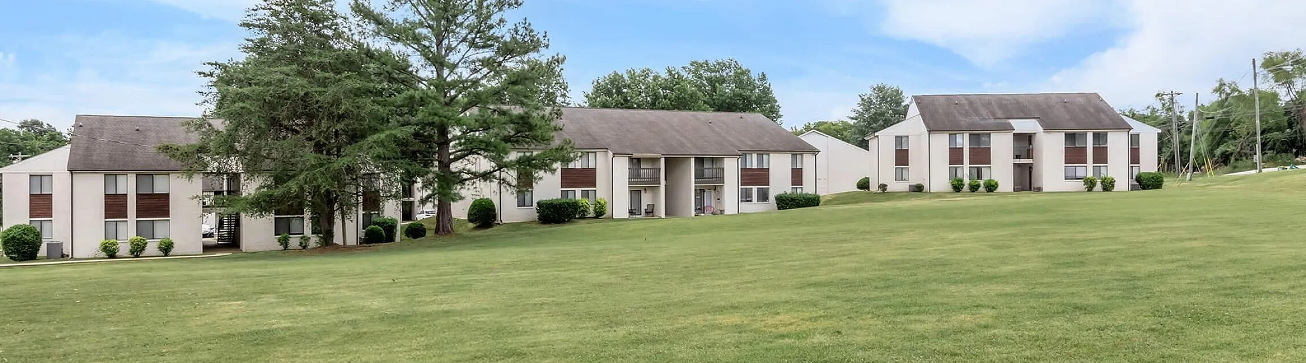 Charming apartment buildings surrounded by lush green lawns and picturesque trees, set under a clear, vibrant sky.