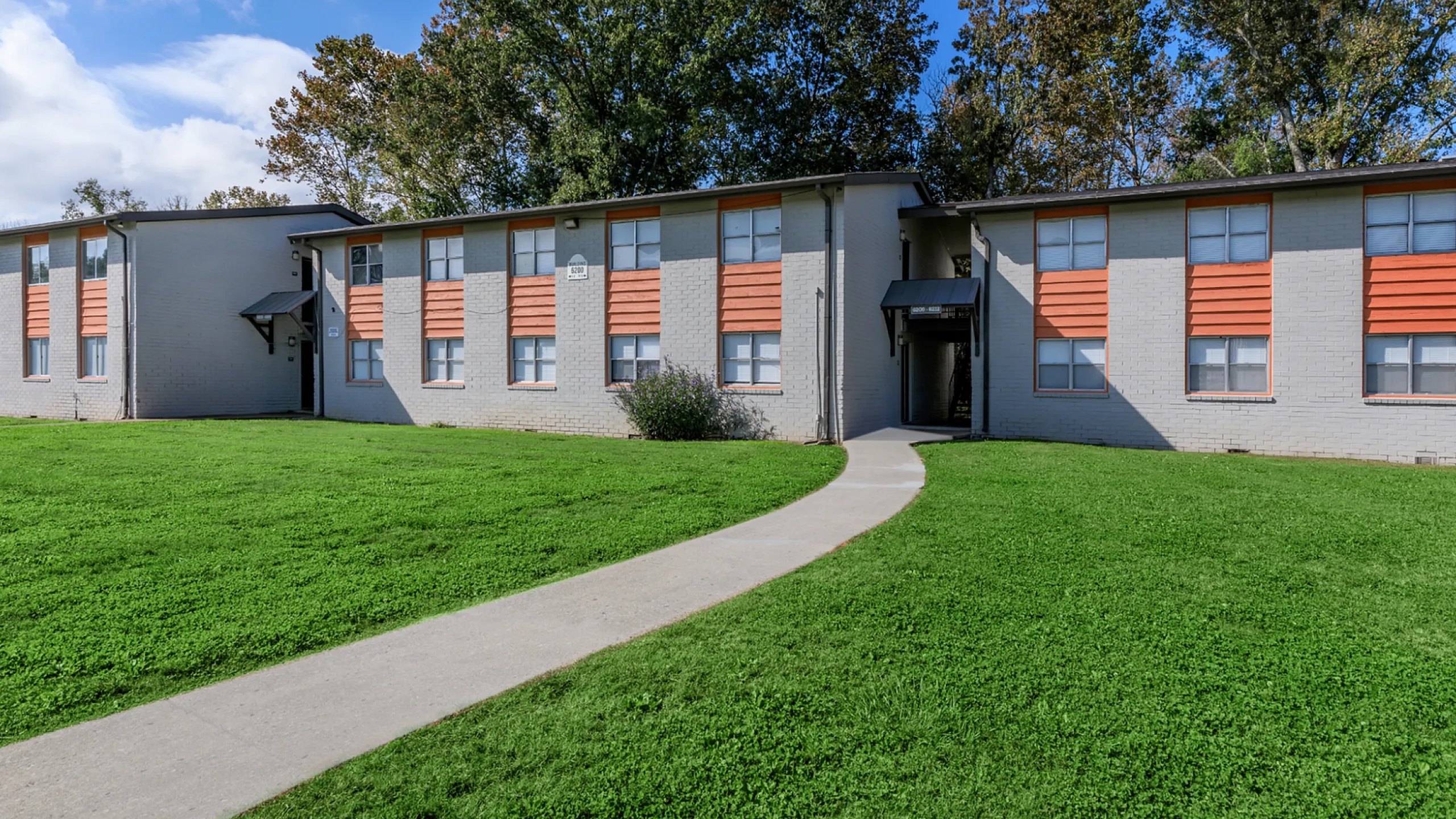 Charming two-story apartment building with a modern facade, surrounded by lush green lawns and mature trees.