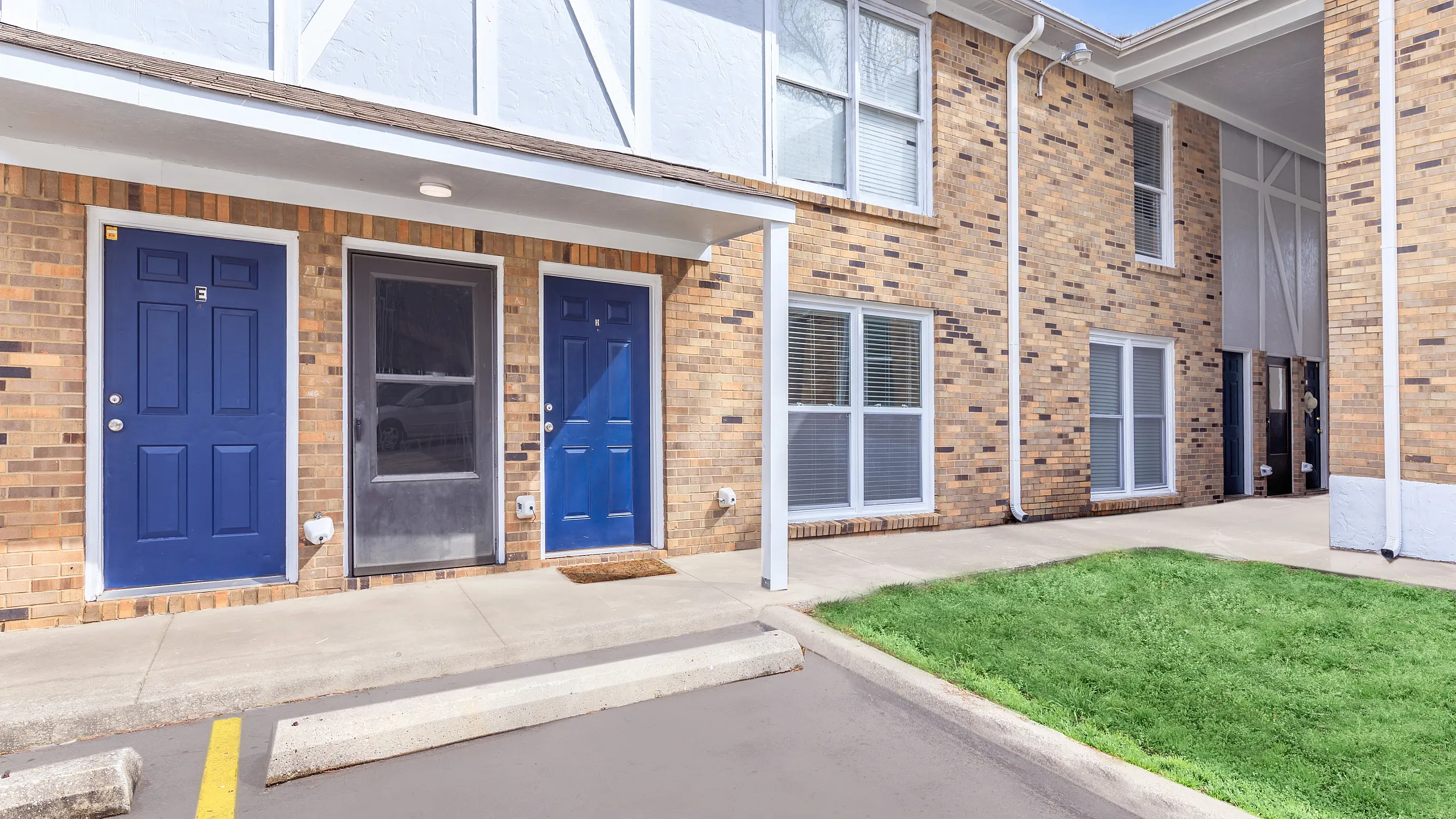 Charming brick exterior of modern apartment building with vibrant blue doors and well-maintained green lawn.