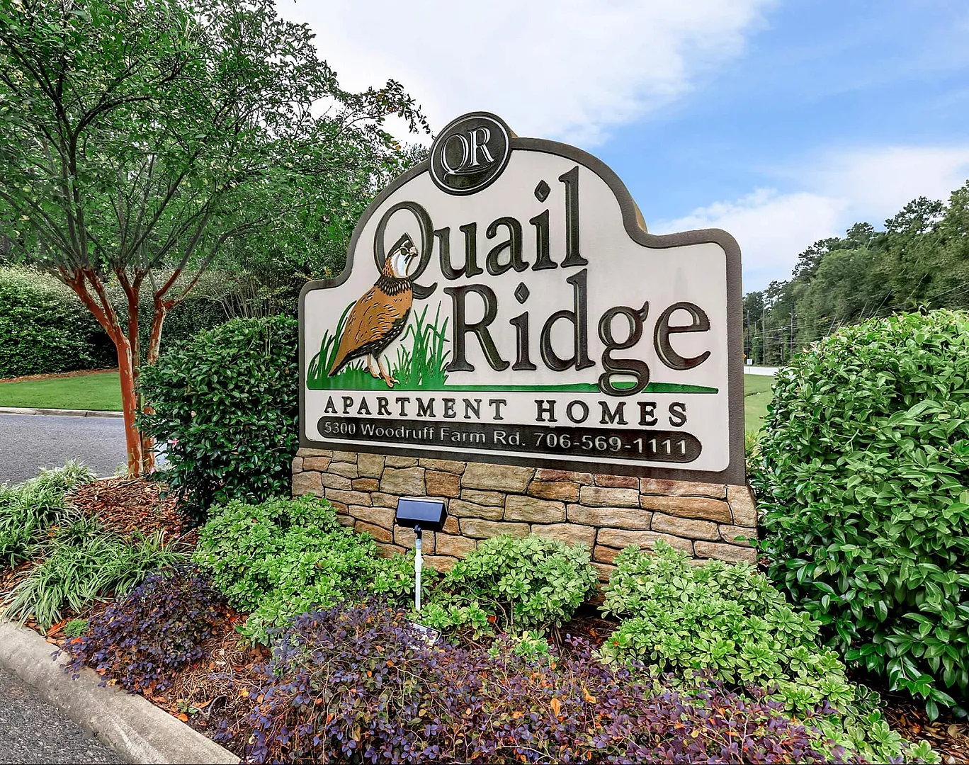 Welcoming entrance sign of Quail Ridge Apartment Homes surrounded by lush greenery and vibrant landscaping.