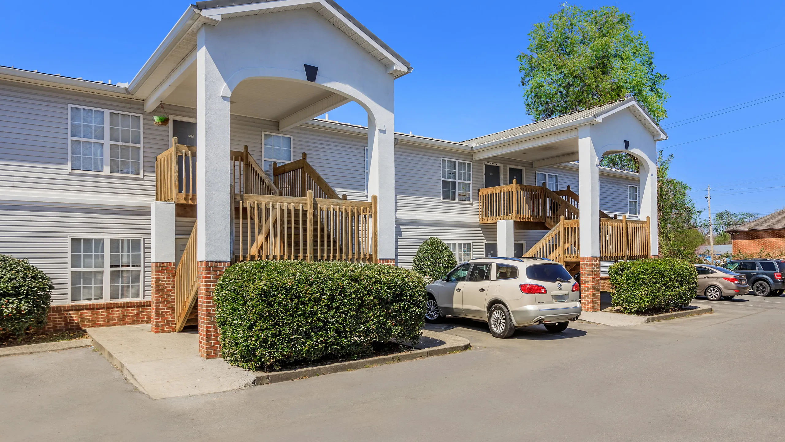 Inviting two-story apartment building with charming wooden staircases and ample parking amidst lush greenery.