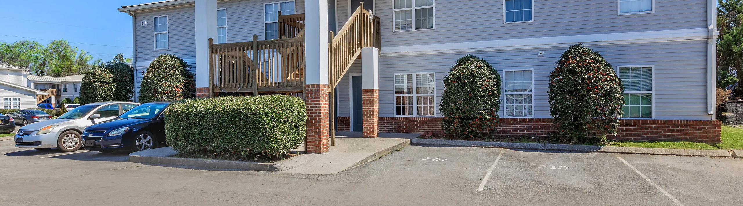 Charming two-story apartment building with welcoming balcony and ample parking set against a clear blue sky.