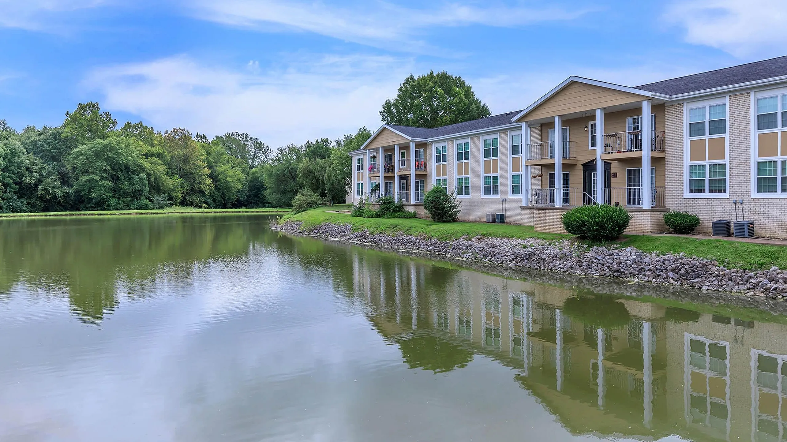 Charming lakeside apartment complex with modern architecture, offering serene water views and lush green surroundings.