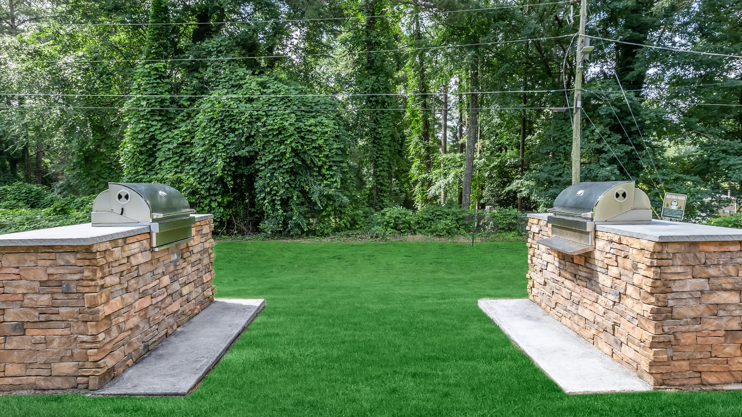 Charming outdoor grilling area with elegant stone countertops nestled in a lush green garden setting.