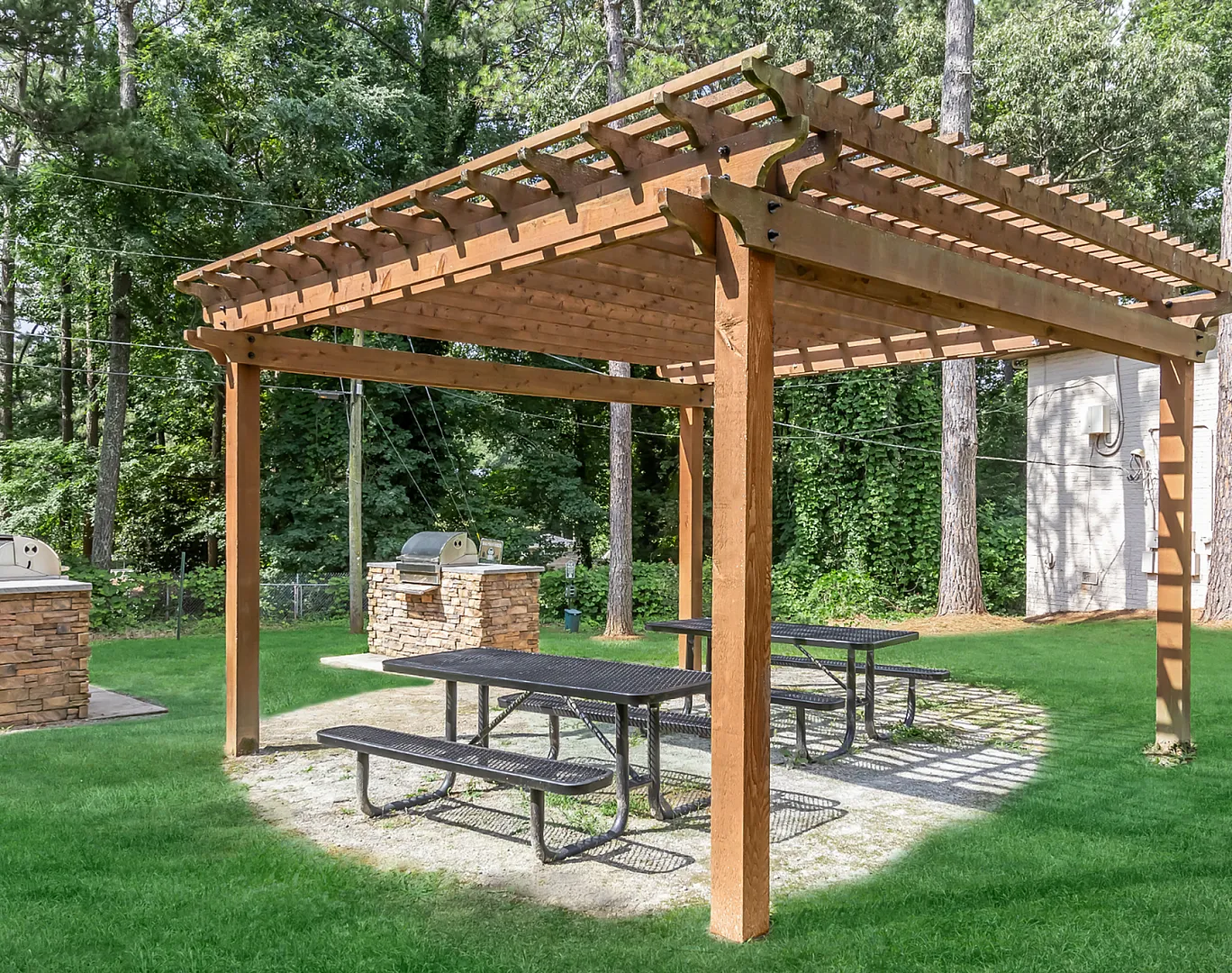 Inviting garden pergola with picnic tables and built-in stone barbecue grills, ideal for outdoor gatherings.