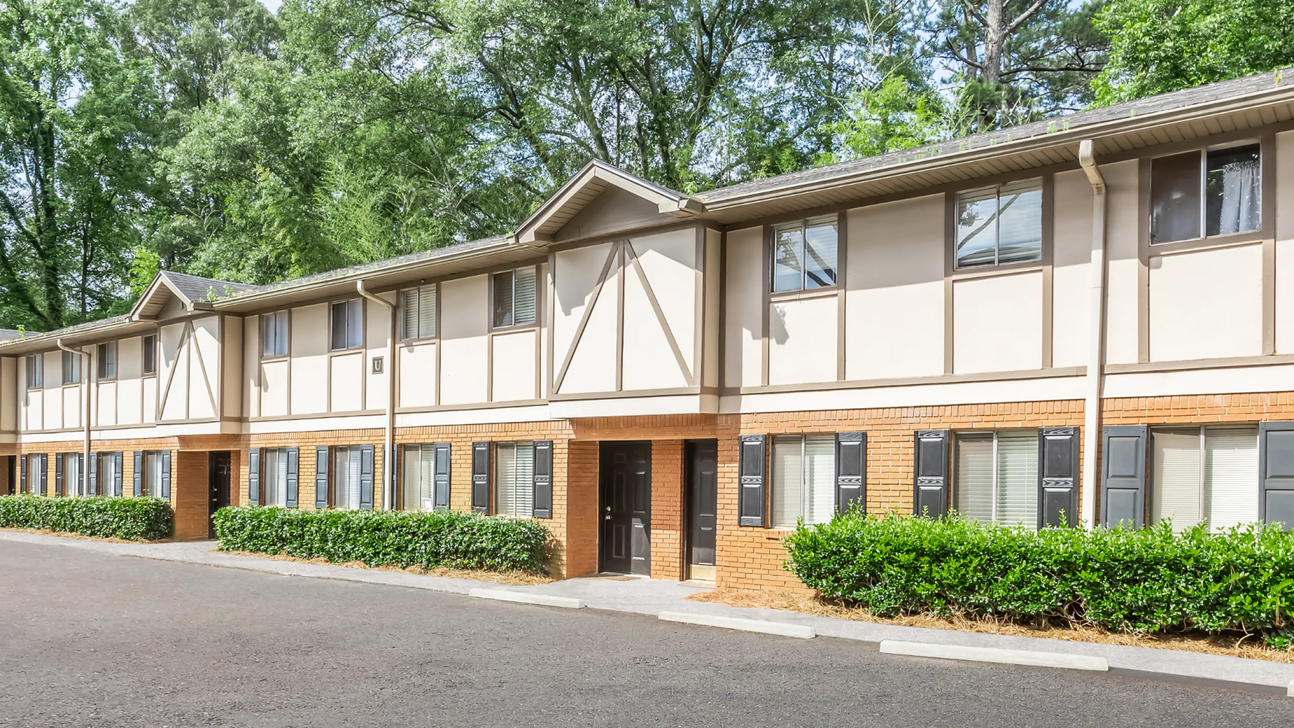 Charming two-story apartment building with classic brick facade and lush greenery, nestled in a serene setting.