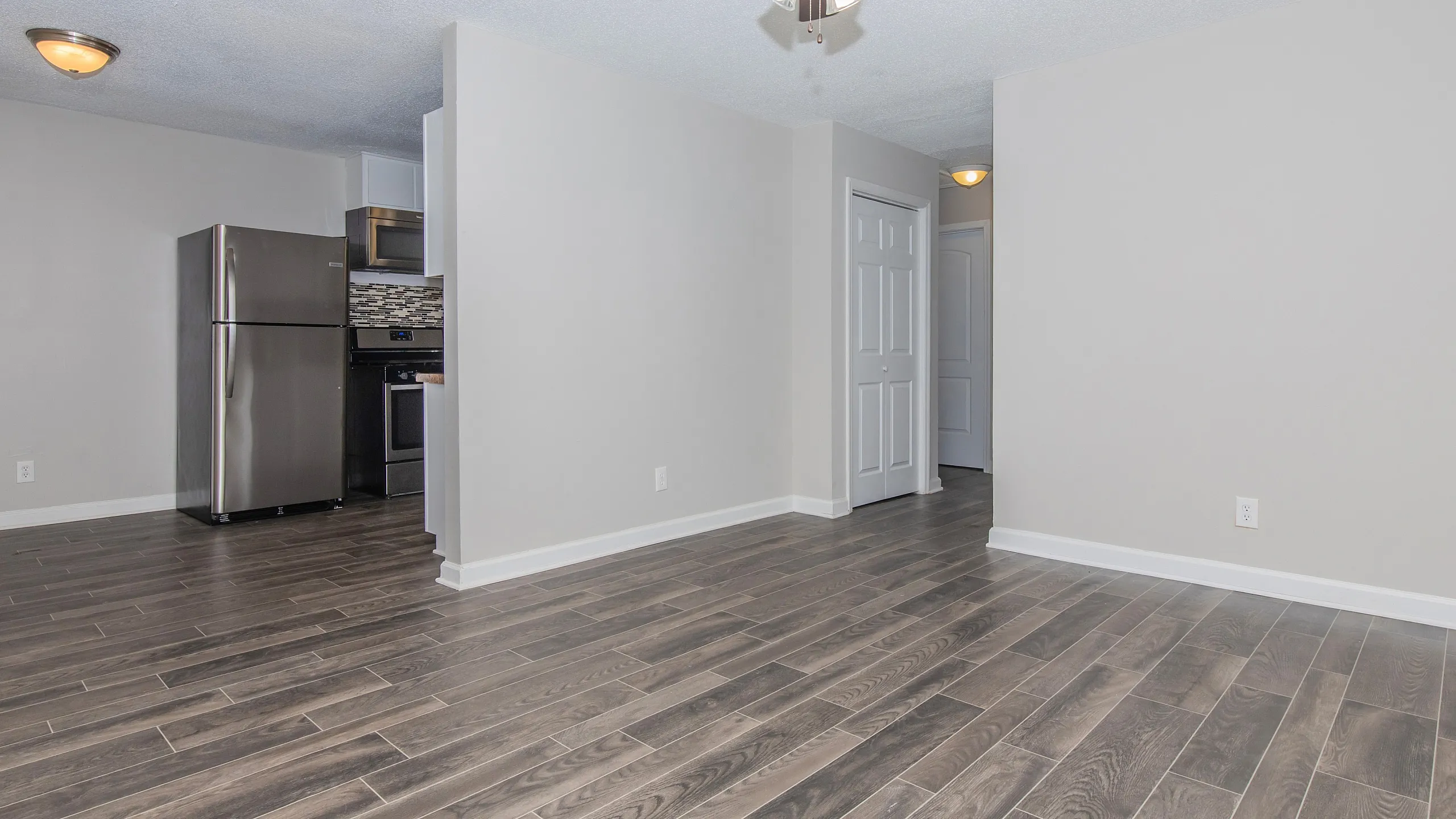 Modern apartment featuring sleek hardwood floors, a stainless steel kitchen with elegant backsplash, and a stylish ceiling fan complementing the open layout.