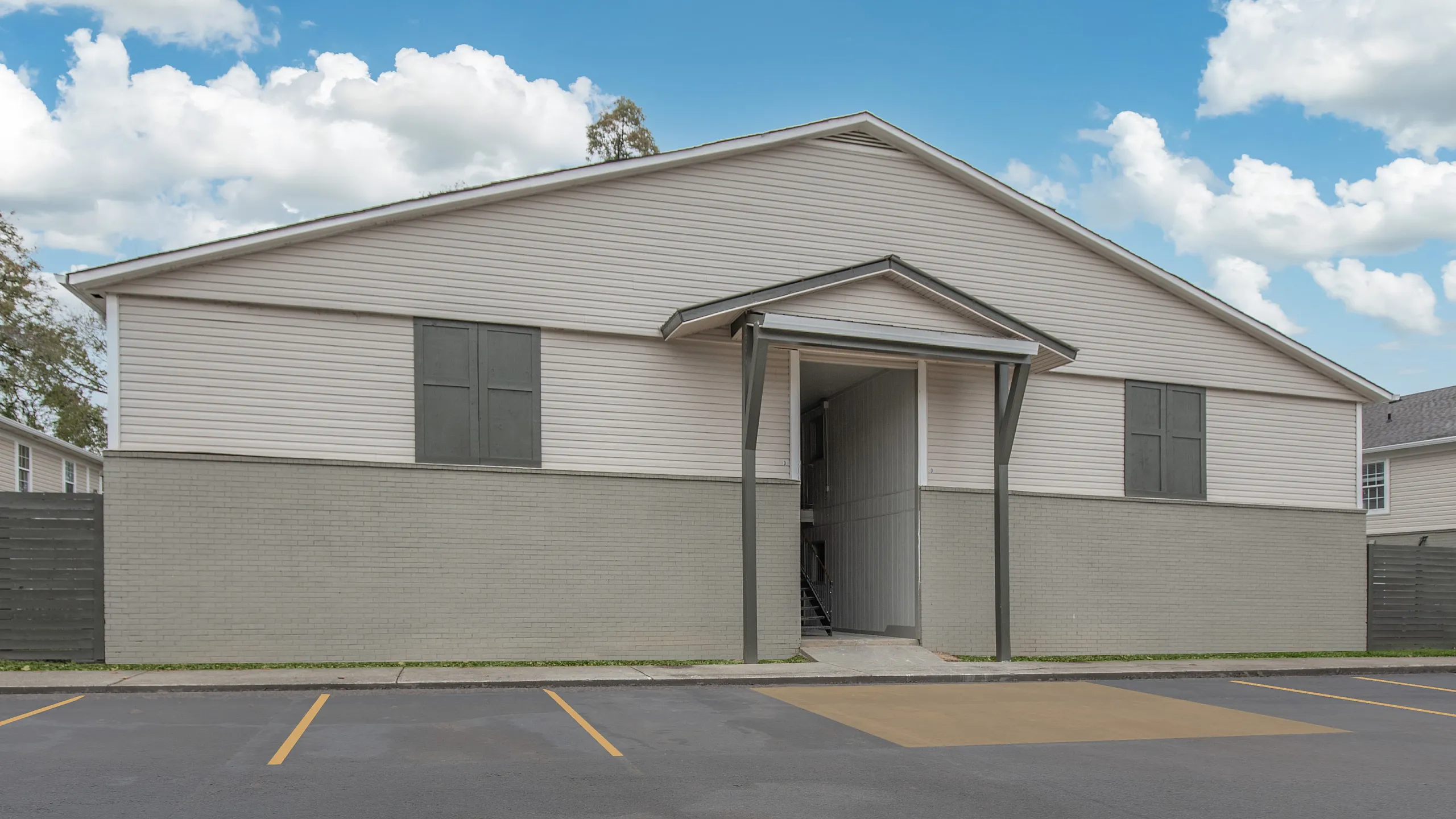 Sleek apartment exterior with modern design, ample parking, and inviting entrance under a clear blue sky.