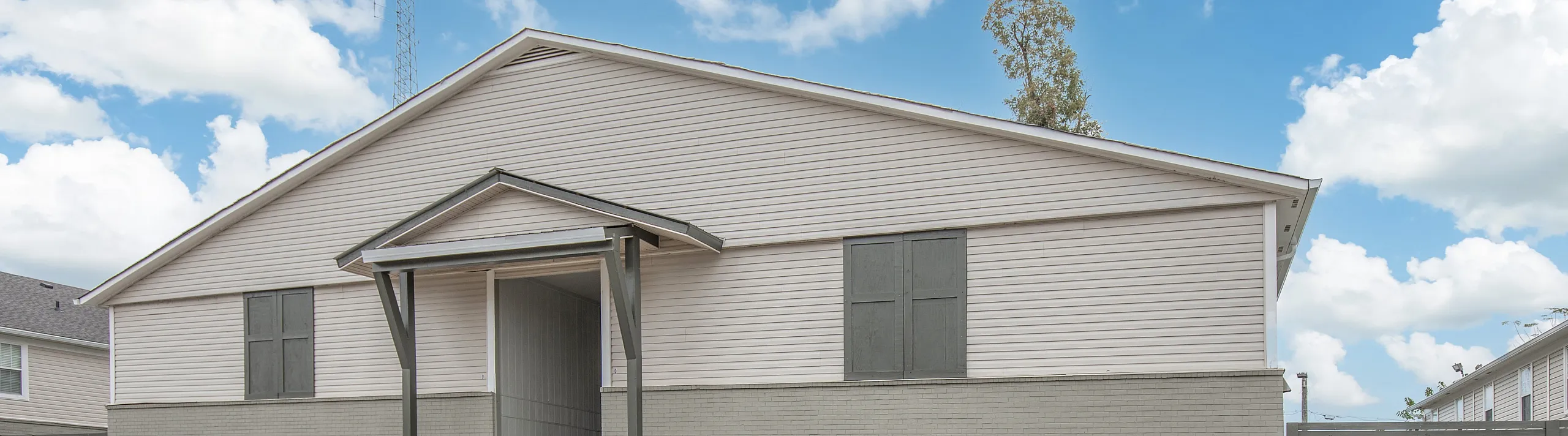 Charming apartment exterior with modern design, ample parking, and a peaceful neighborhood backdrop under a bright blue sky.