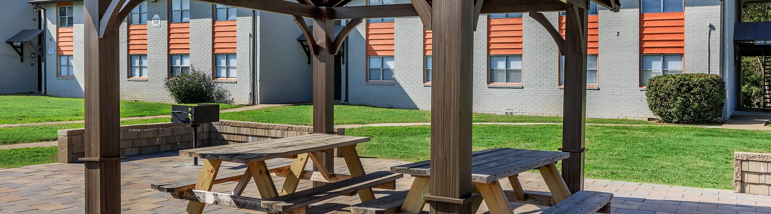 Charming outdoor space with a modern pergola and picnic tables, perfect for relaxing or social gatherings in a lush apartment courtyard.