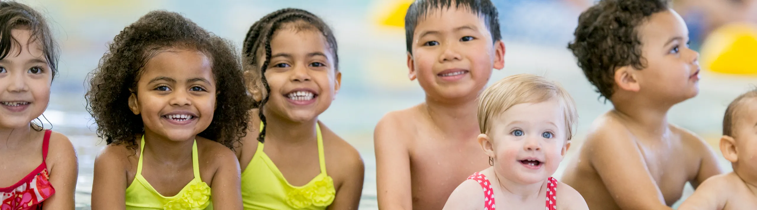 Group of joyful children in colorful swimwear enjoying a fun day at the pool, smiling cheerfully.