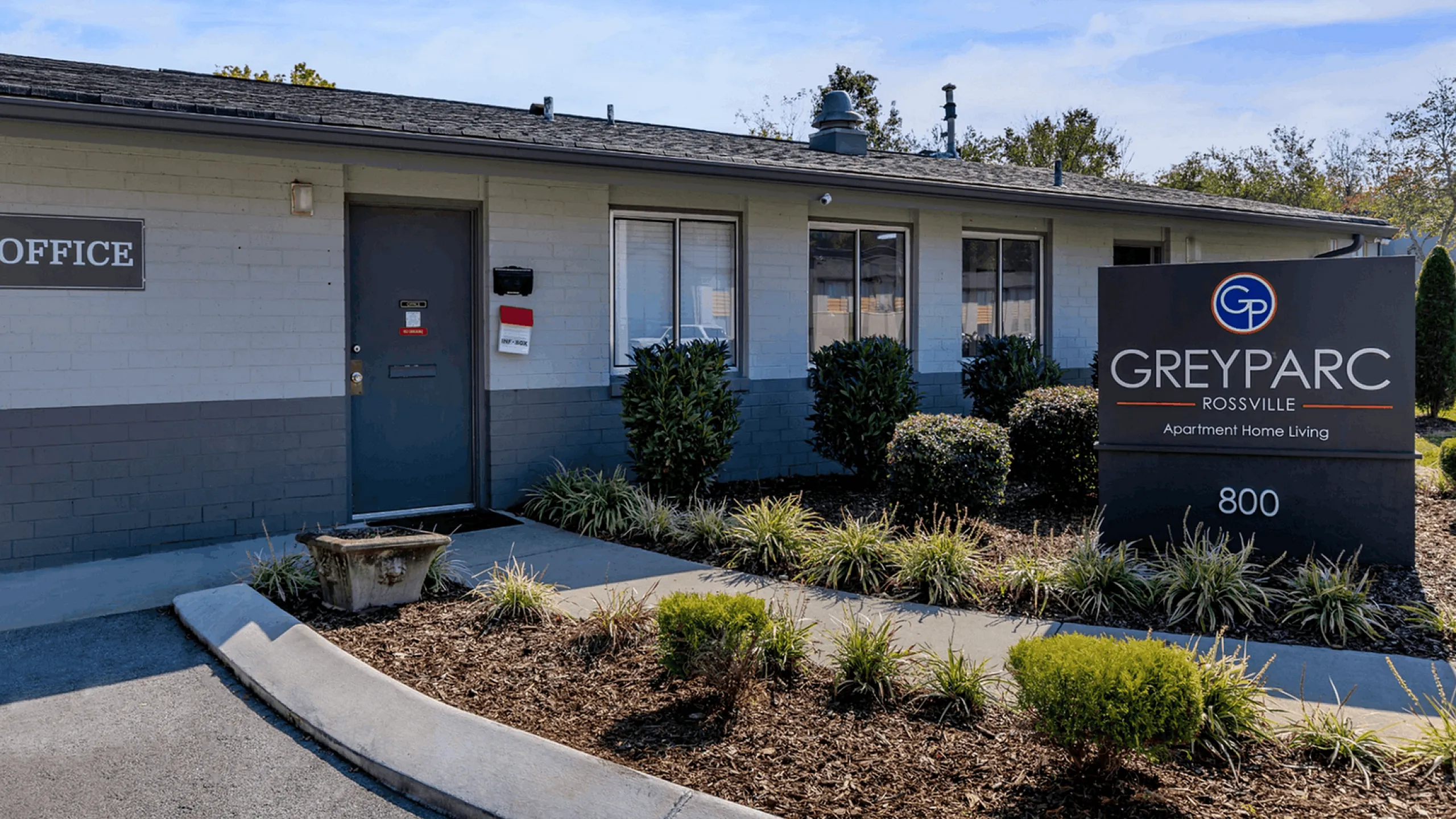 Welcoming GreyParc Rossville apartment office entrance with manicured landscaping and contemporary signage.
