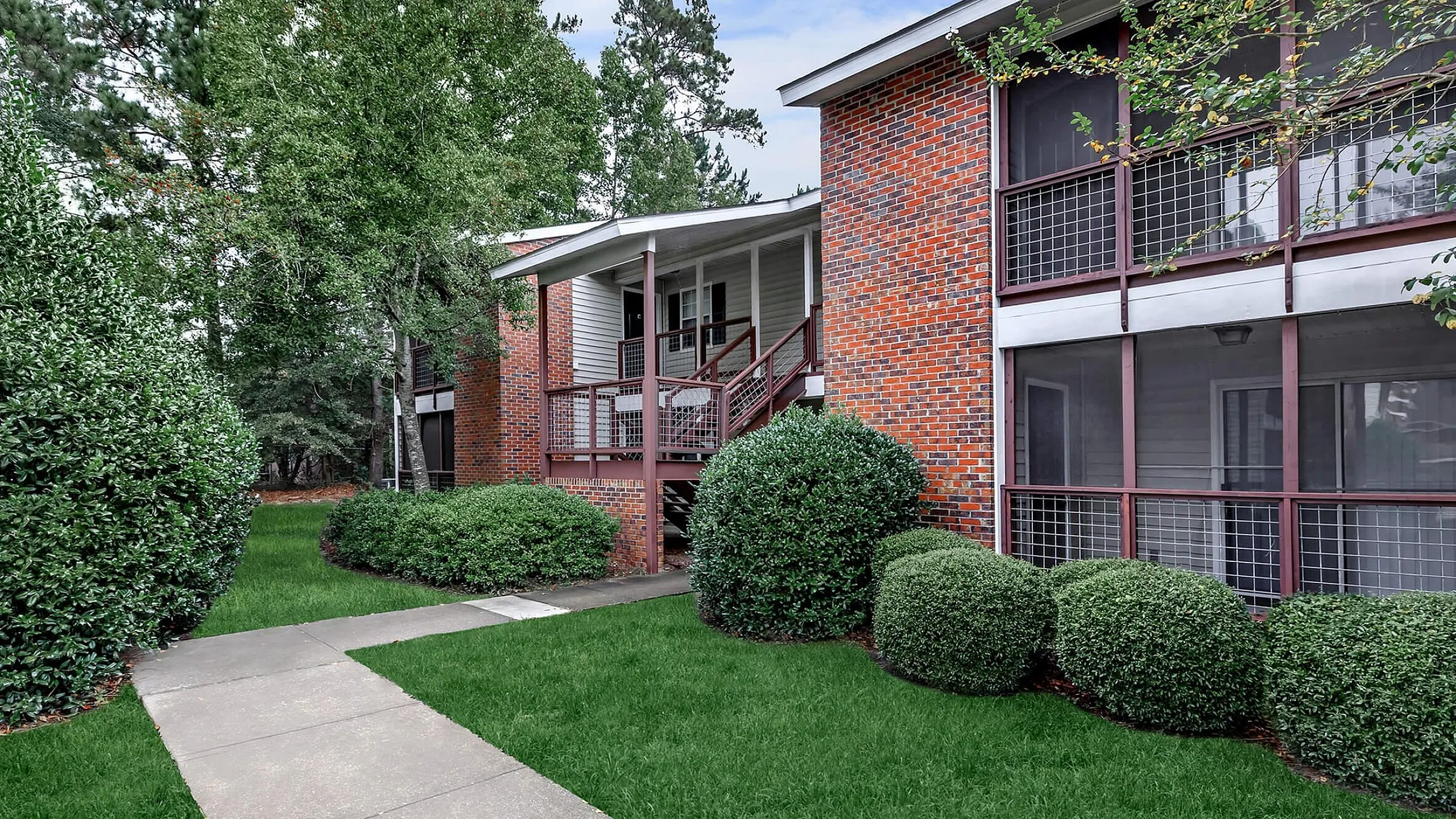 Charming brick apartment building with lush green landscaping and cozy balconies, offering a peaceful living environment.
