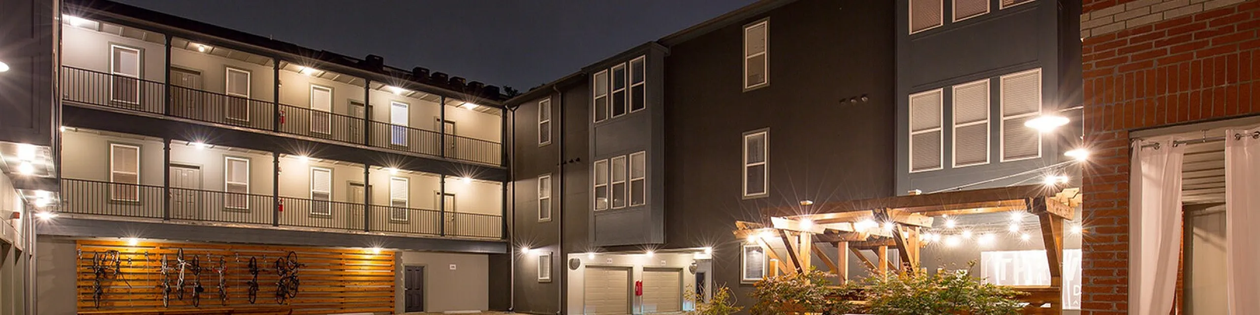Chic urban apartment complex with warm night lighting, featuring a stylish courtyard and modern architecture.