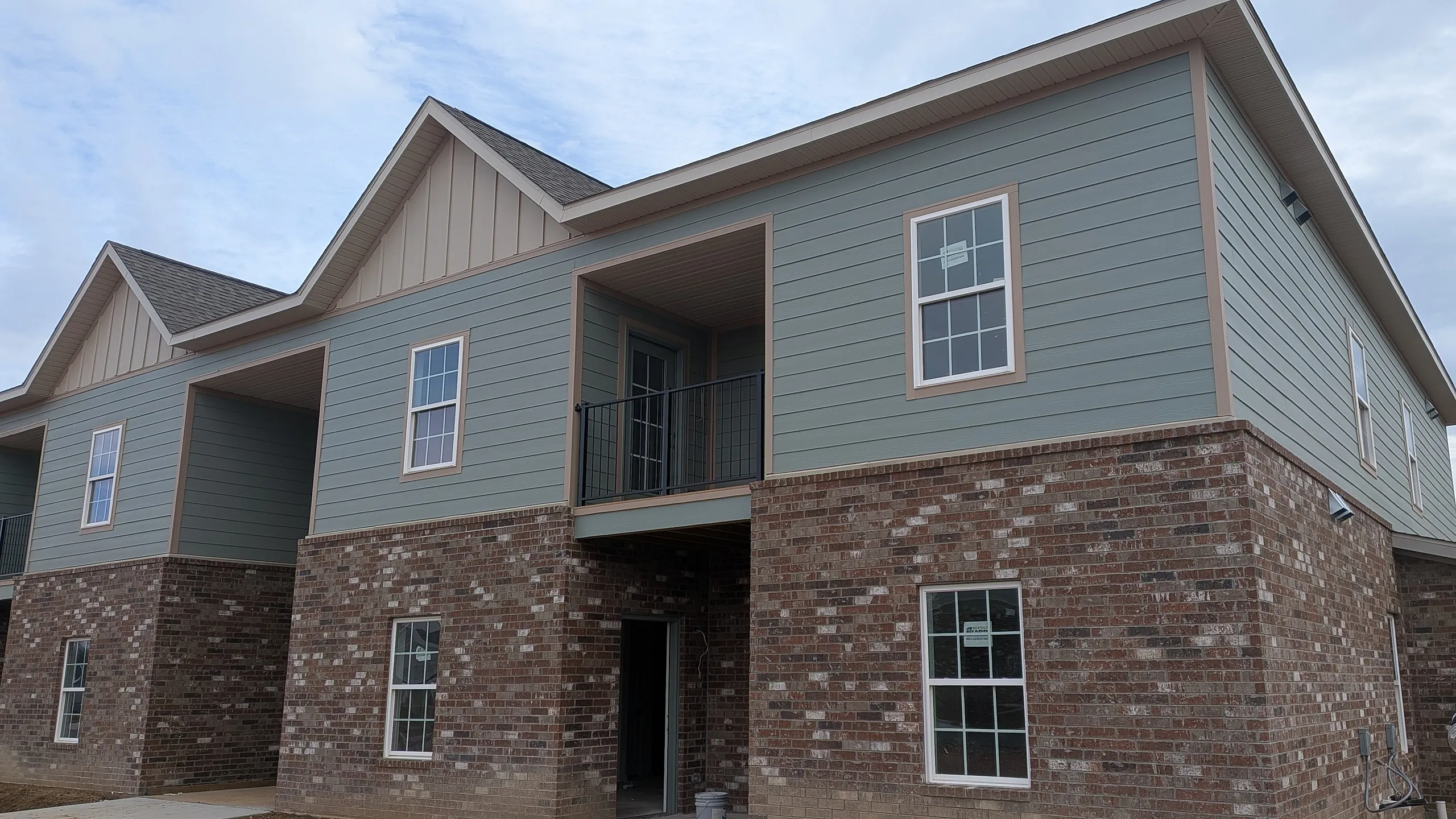 Charming two-story apartment building with brick and siding exterior, featuring spacious balconies and large windows under a beautiful blue sky.