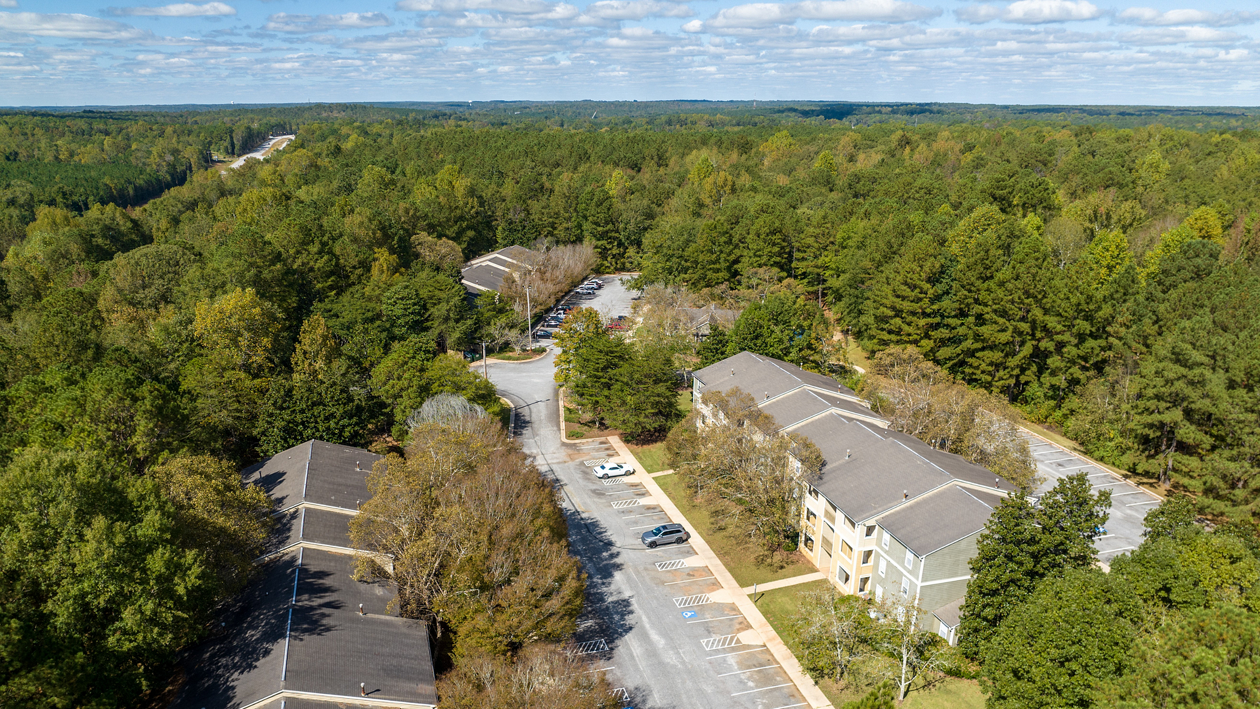 Aerial view of serene apartment complex surrounded by lush green forests, offering a peaceful living environment and ample parking spaces.