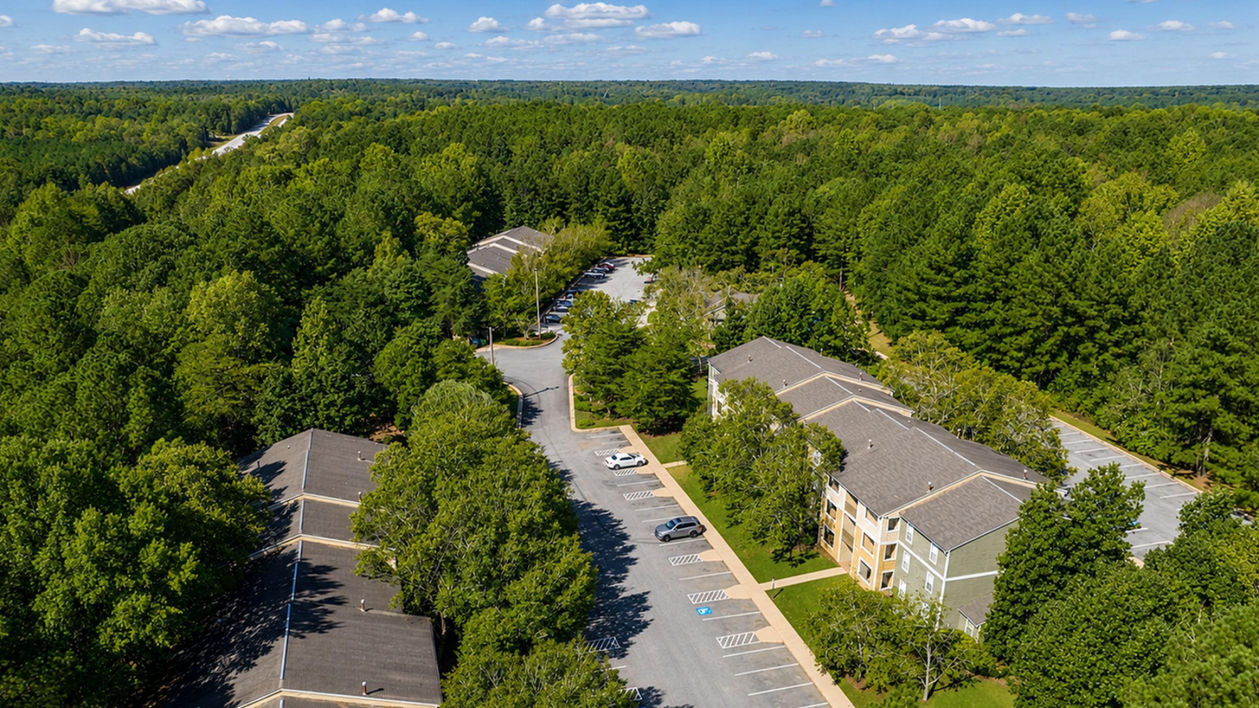 Breathtaking aerial view of modern apartment complex nestled in lush greenery, offering ample parking and serene surroundings.