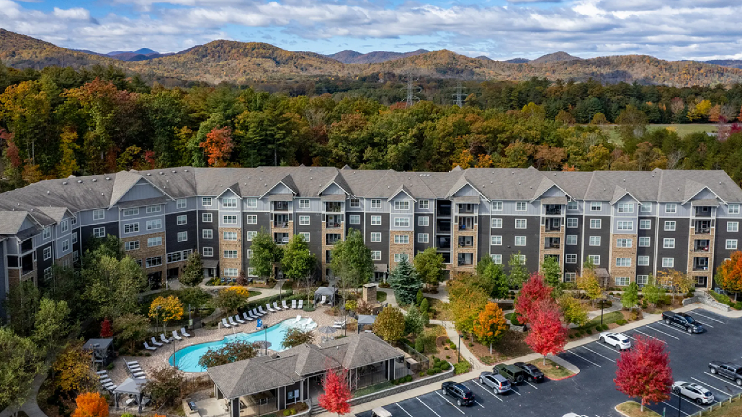 Elegant apartment complex nestled in vibrant autumnal landscape, featuring a sparkling pool and scenic mountain backdrop.