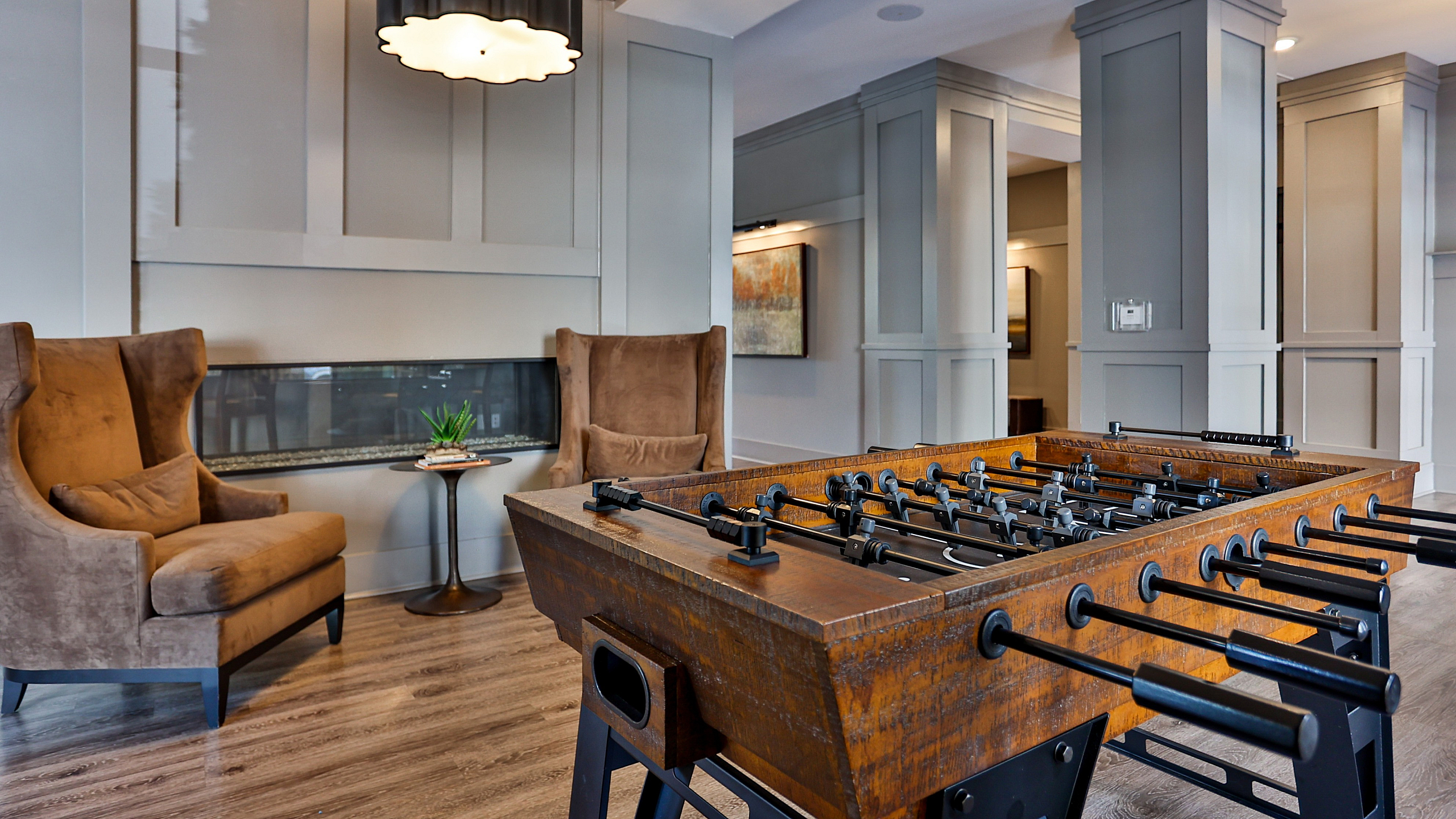 Chic lounge area with comfortable velvet chairs and stylish foosball table, accented by modern paneling and ambient lighting.