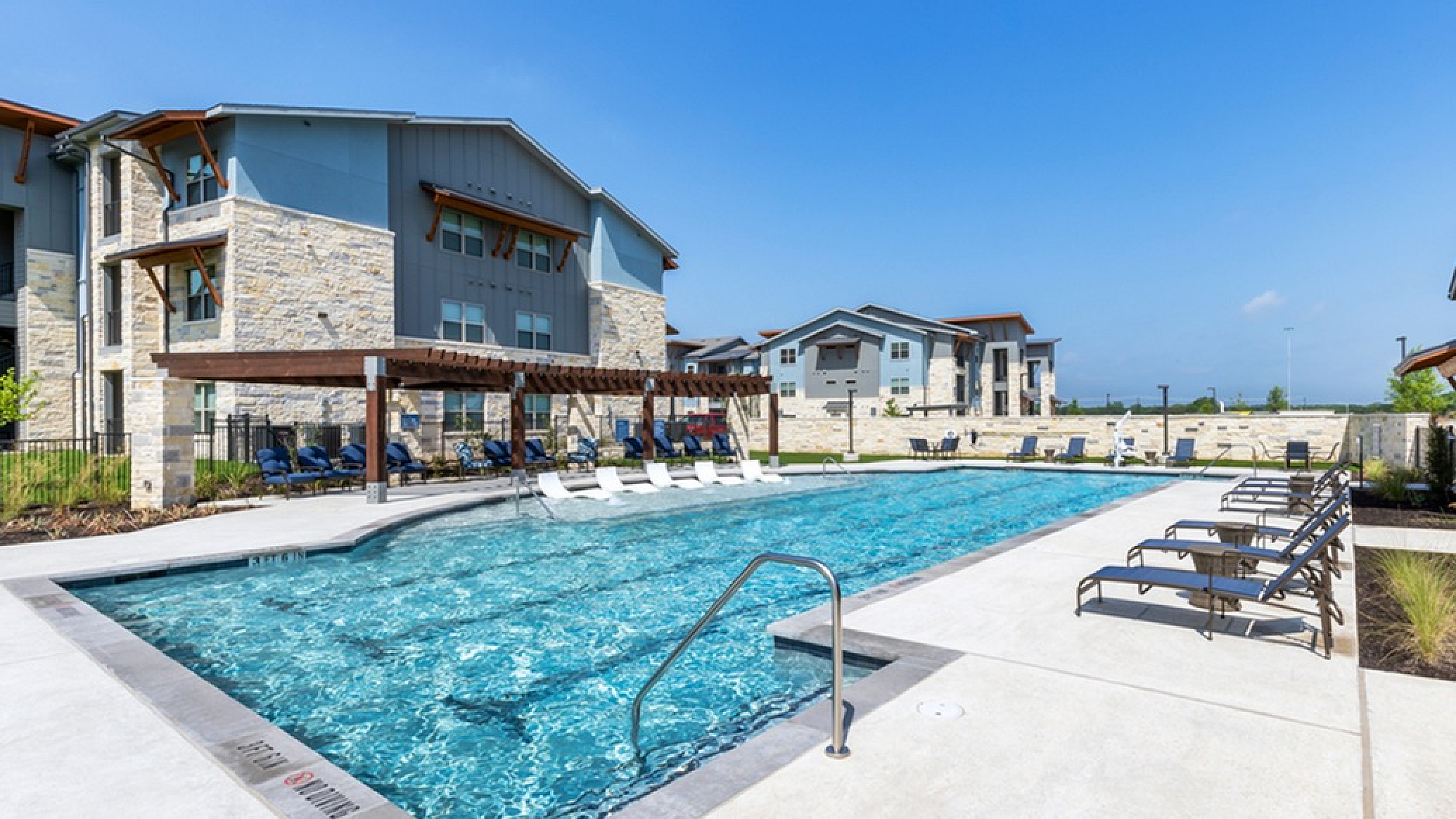 Luxurious apartment complex featuring a sparkling outdoor pool with stylish lounge chairs and modern architecture.