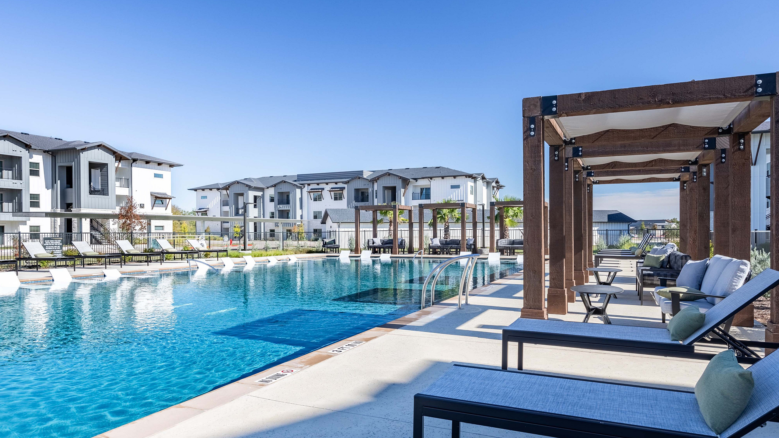 Luxurious apartment complex with a stunning outdoor pool, stylish loungers, and pergola-covered seating areas.