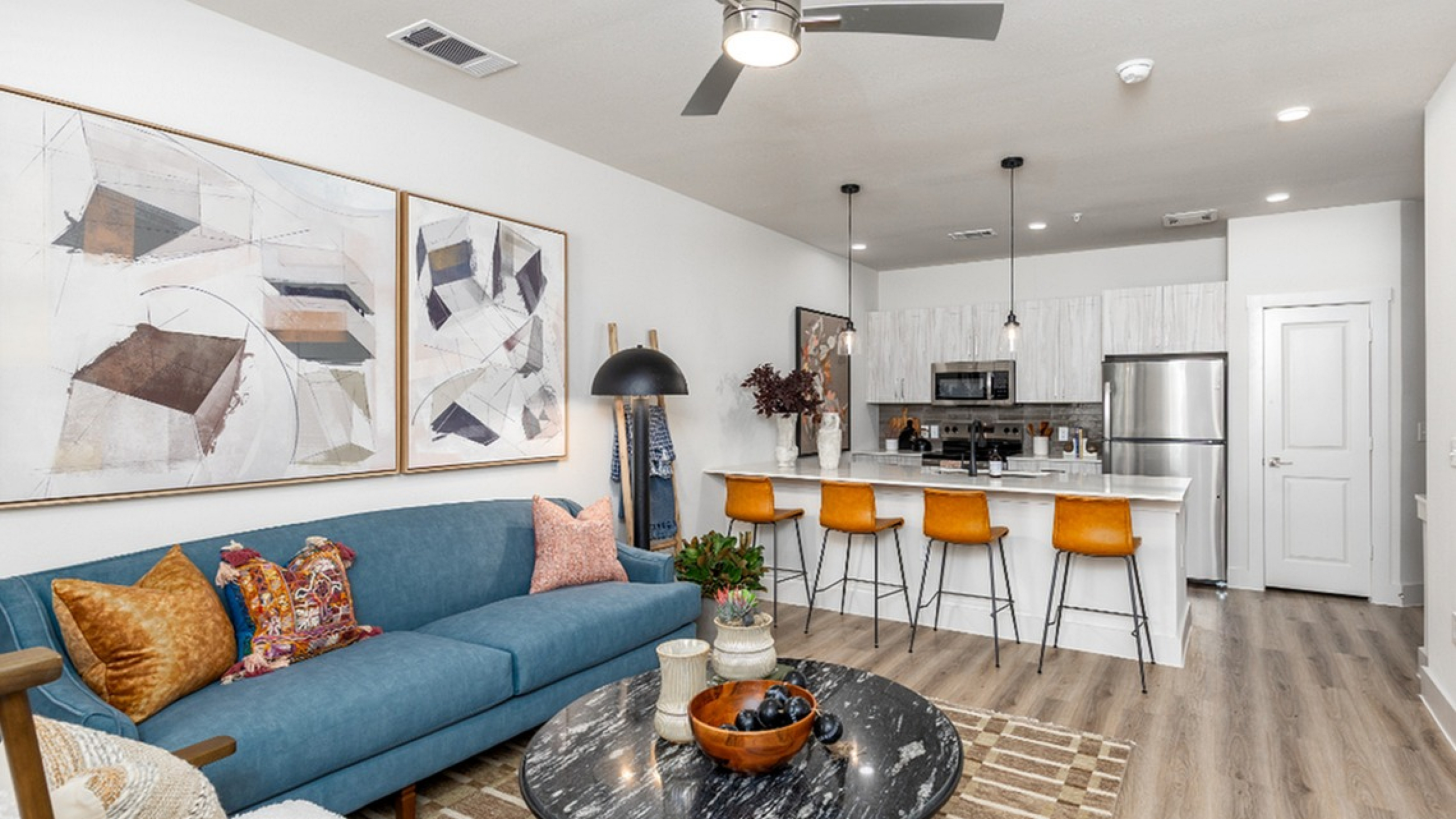 Modern open-concept living room with chic decor, featuring a stylish blue sofa, artistic wall art, and a sleek kitchen island with bar stools.