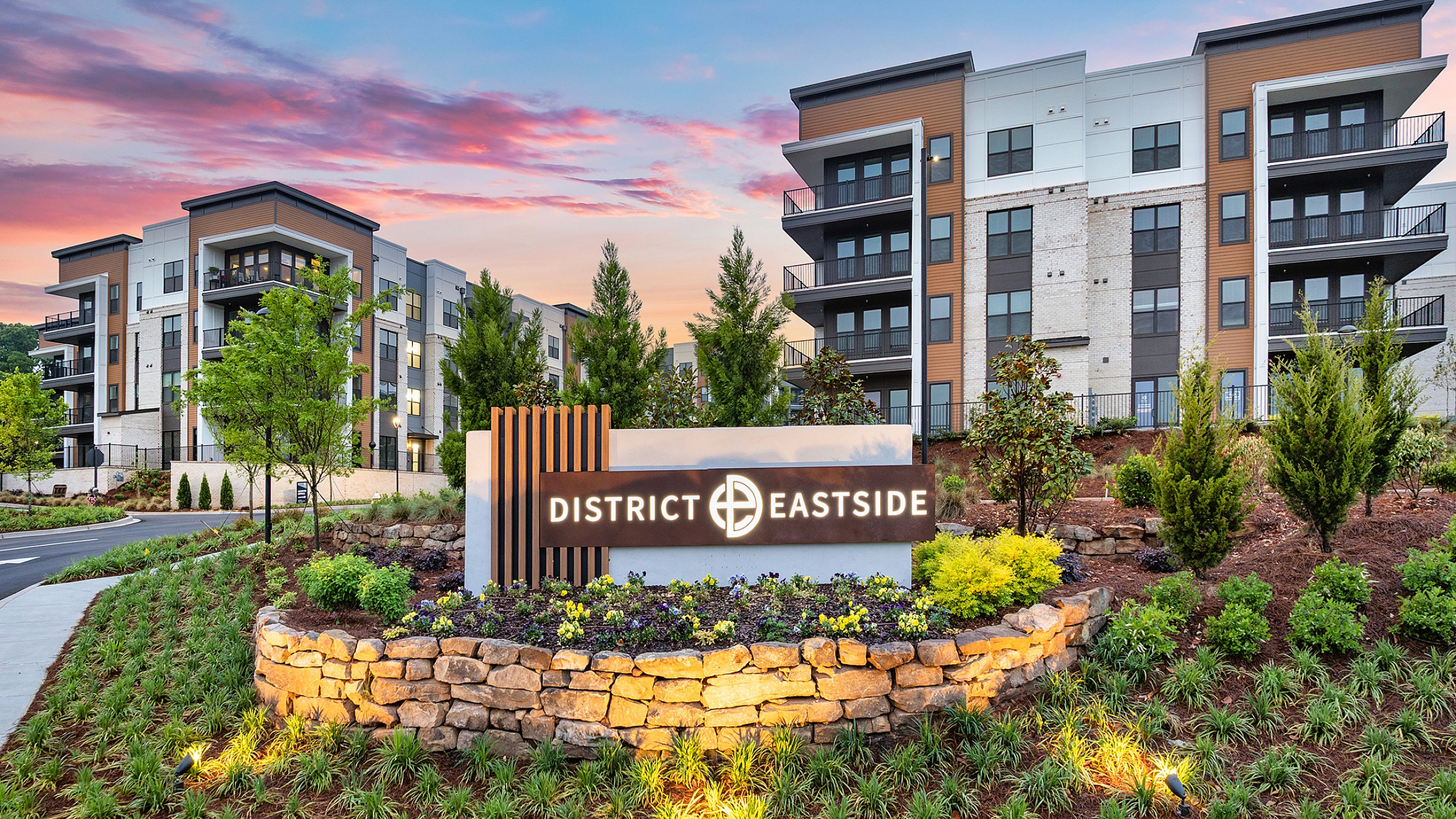 Elegant modern apartment complex with lush landscaping at District Eastside, featuring stylish architecture and vibrant greenery under a picturesque evening sky.