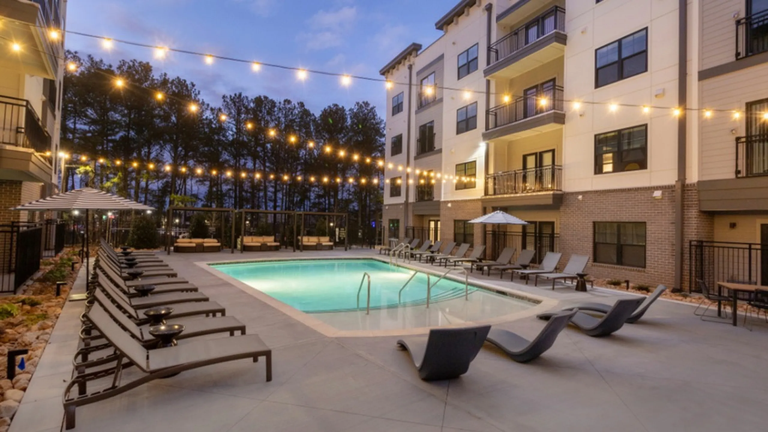 Modern apartment complex with illuminated pool and lounge chairs, perfect for evening relaxation.