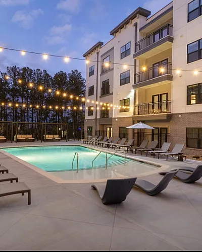 Luxurious apartment complex featuring a stunning outdoor pool with elegant lounge chairs, ambient string lighting, and modern architecture.